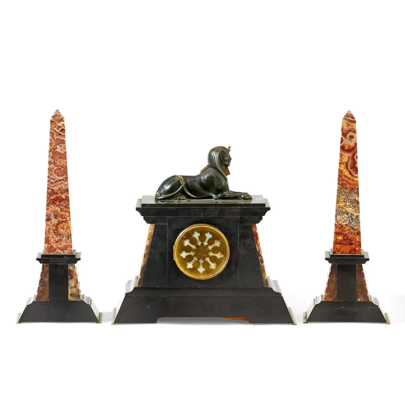 Egyptian revival mantel clock & garniture set, early 20th century.
 
Circular white sunken dial with black Arabic numerals and brass sunburst with two train movement set in a polished black slate and stepped rouge marble case decorated with