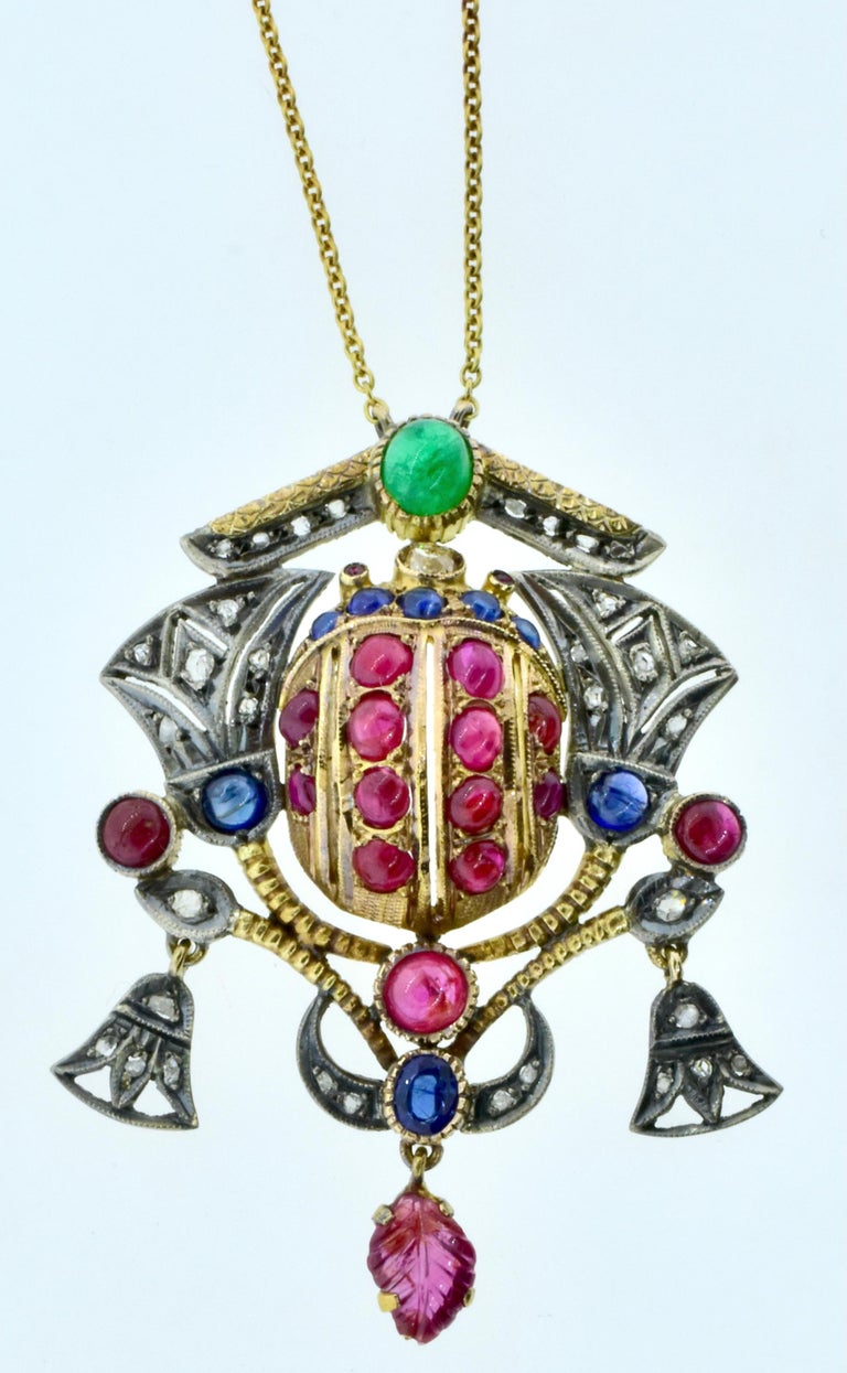 Egyptian revival pendant necklace, silver topped 18K gold and centering a scarab studded with natural rubies.  Lotus motifs set with rose cut diamonds and cabochon cut natural sapphires flank the center scarab creating an expressive pendant. 