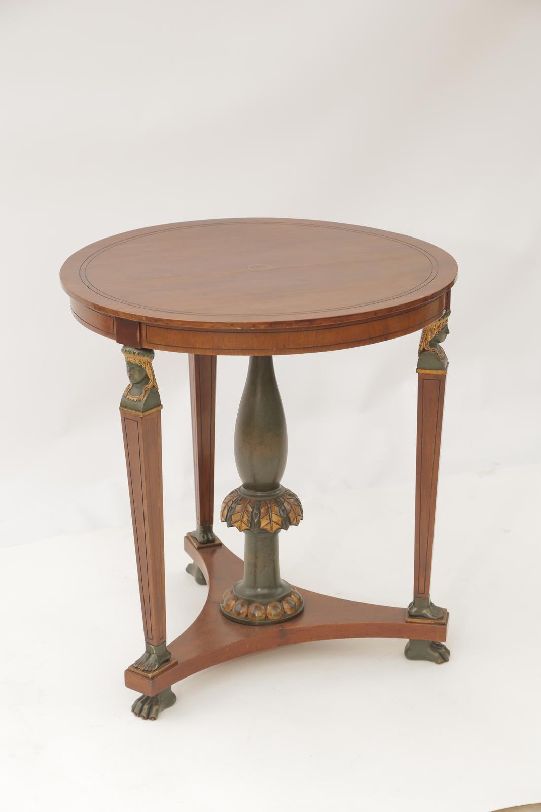 Unusual table, of rosewood with polychrome accents, having a round top accented by a brass ring, raised on a trio of herms as legs, each surmounted by an Egyptian torso, and ending in a pair of feet, on a concave tripartite plinth, with a turned and