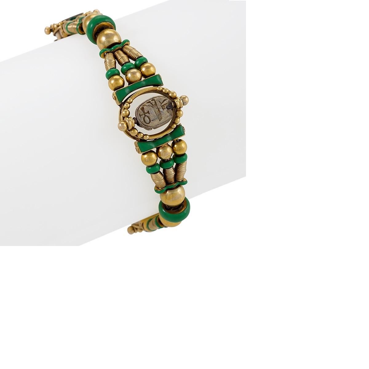 An Egyptian Revival bracelet, circa 1860, in 18 karat gold with green enamel framing and beads. The bracelet features three faience scarabs; two smaller, flanking insects in teal, and one large scarab in earthen tones at the center of the piece.