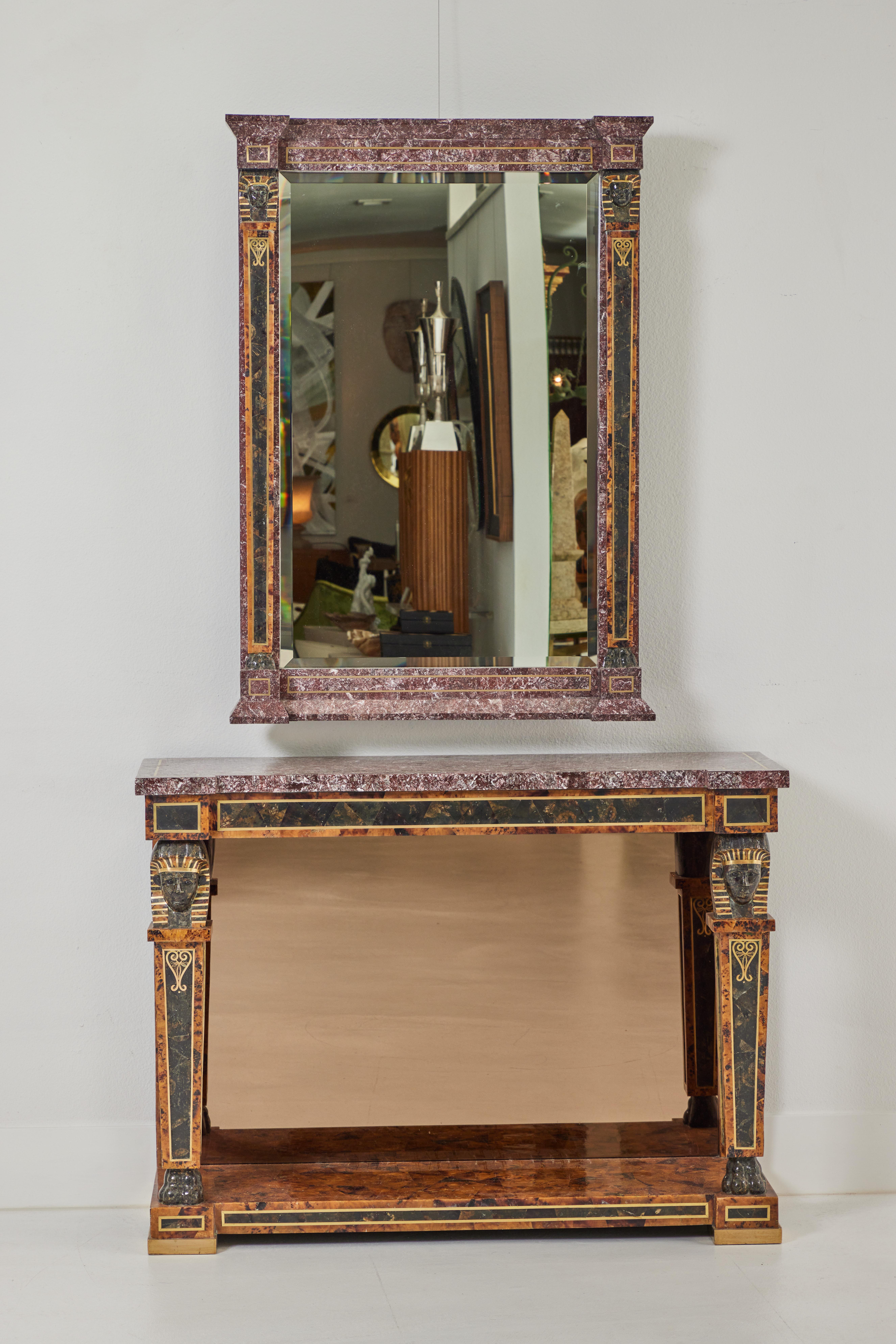 This Egyptian Revival style console and mirror features tesselated stone and shell with brass inlays. Made by Maitland Smith in the 1980s, the console enhanced with Sphinx heads above the front legs and brass inlays veneered in a combination of both