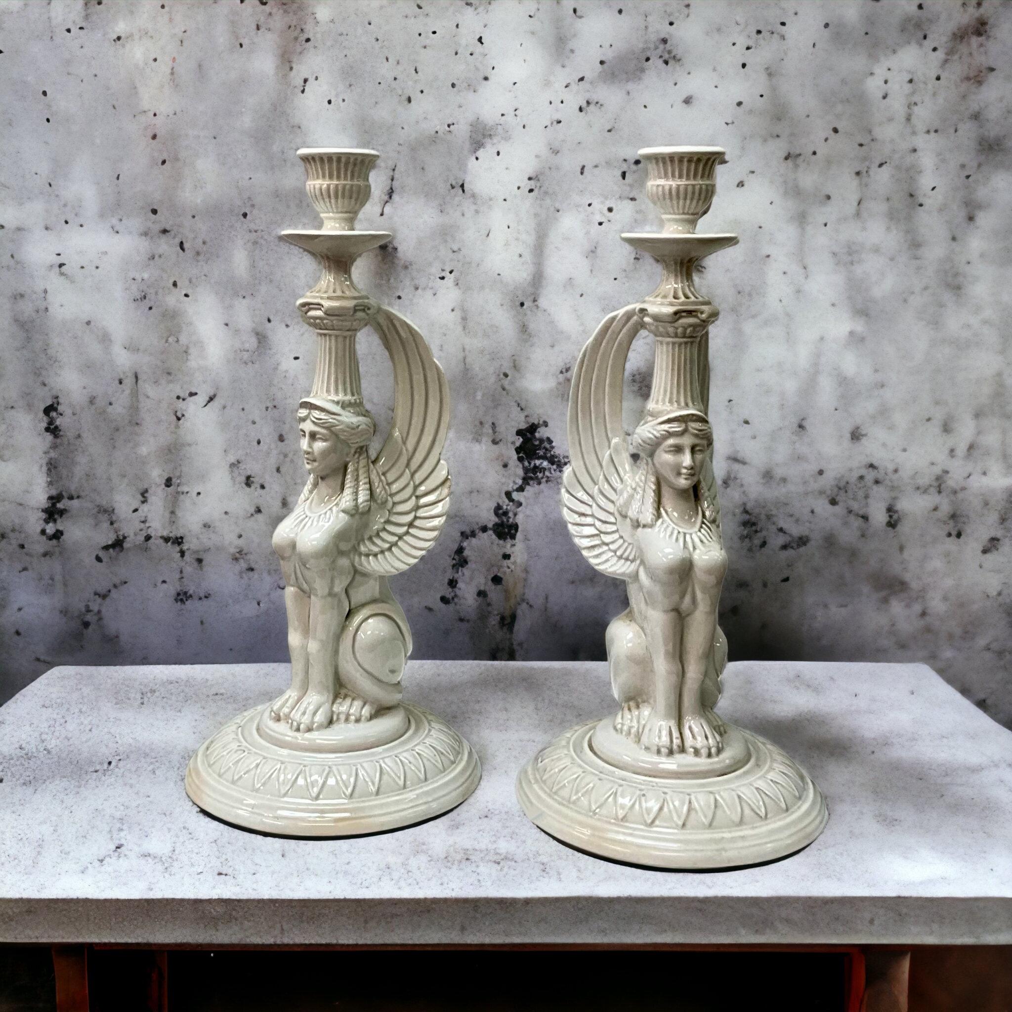 This is a pair of Egyptian Revival style Fitz and Floyd white porcelain candlesticks. They date to the 70s and were crafted in Japan. They are marked. 