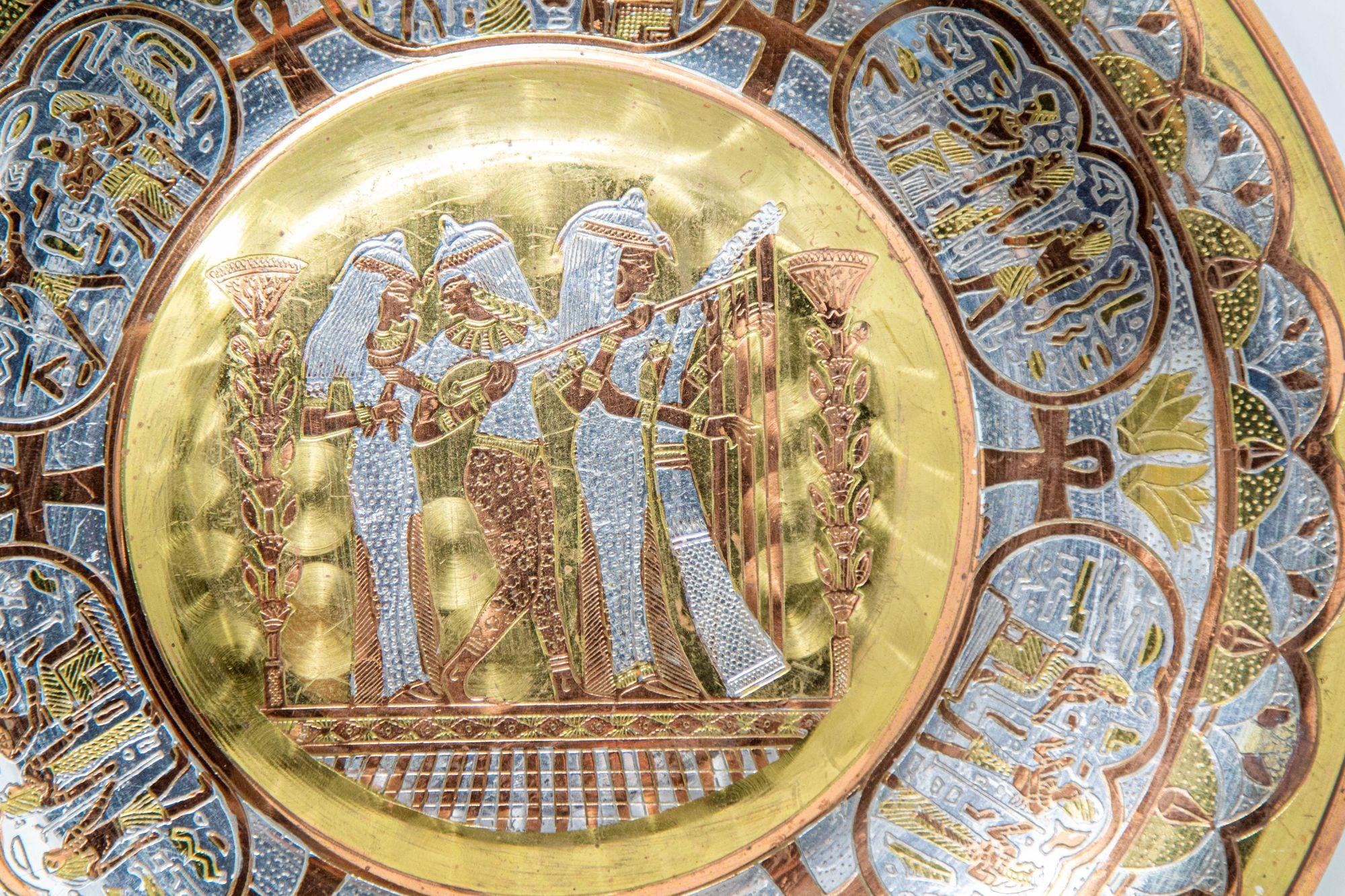 Egyptian Revival Round Brass Tray with Silver and Copper Overlay Wall Hanging.
Dimensions: 8.75 in. diameter.
Label in the back with the Artist Name: Mohamed El Zareif, handmade in Egypt.
Circa 1970.
Vintage Wall Hanging Egyptian decorative