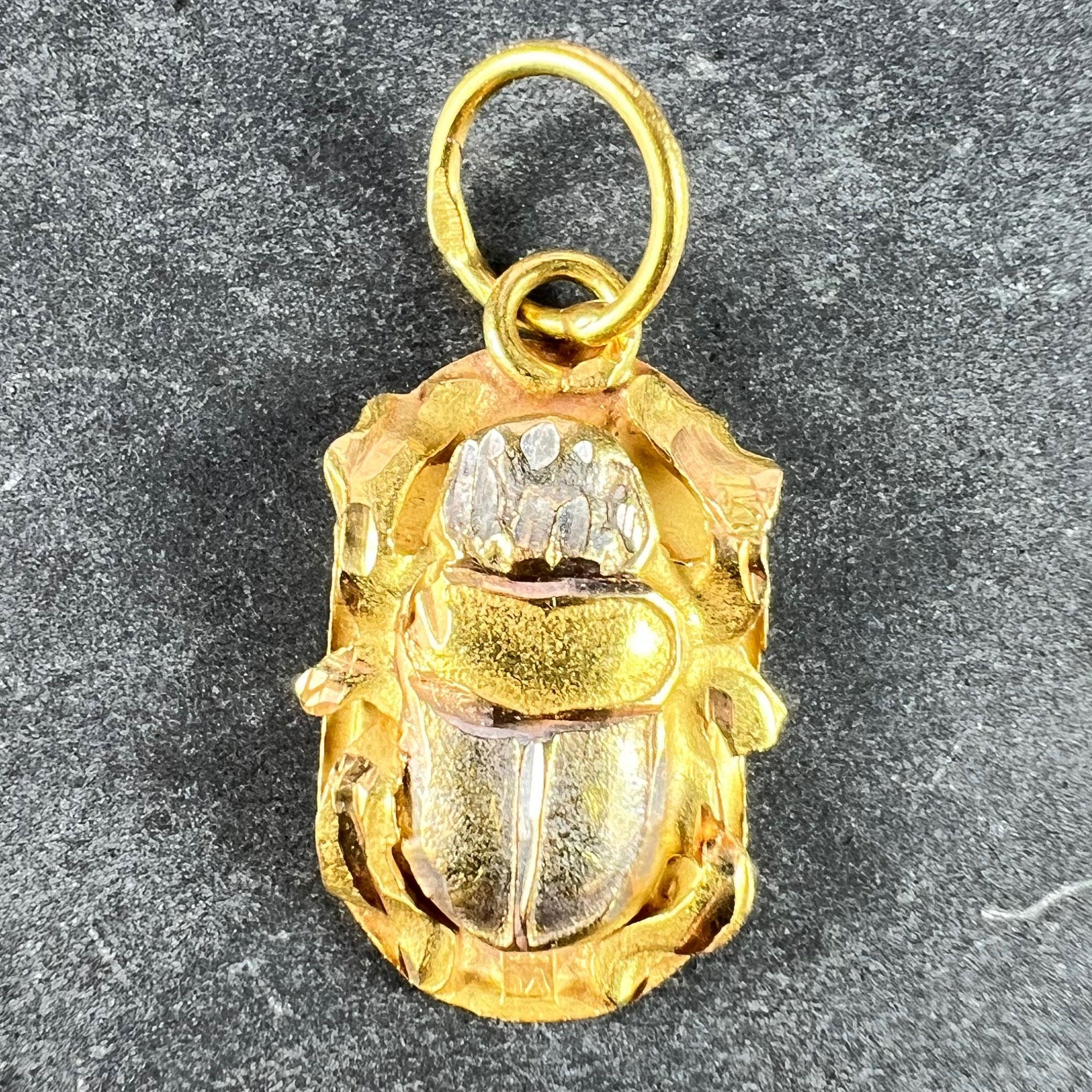 An Egyptian 18 karat (18K) yellow and white gold charm pendant designed as the protective amulet of an Egyptian scarab, with a relief of a scarab beetle holding up the sun to the reverse in a cartouche. Stamped with the Egyptian mark for 18 karat