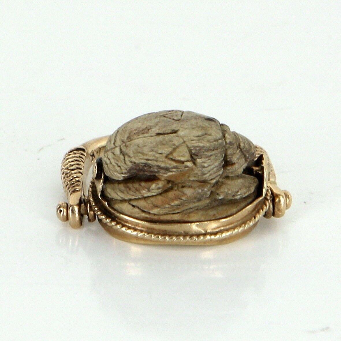 Ornate Egyptian scarab beetle ring (circa 1960s), crafted in 14 karat yellow gold. 

Centrally mounted brown stone is hand carved in the form of a scarab beetle. The side mounts are hinged to allow the ring to move forwards or backwards (or 'flip').