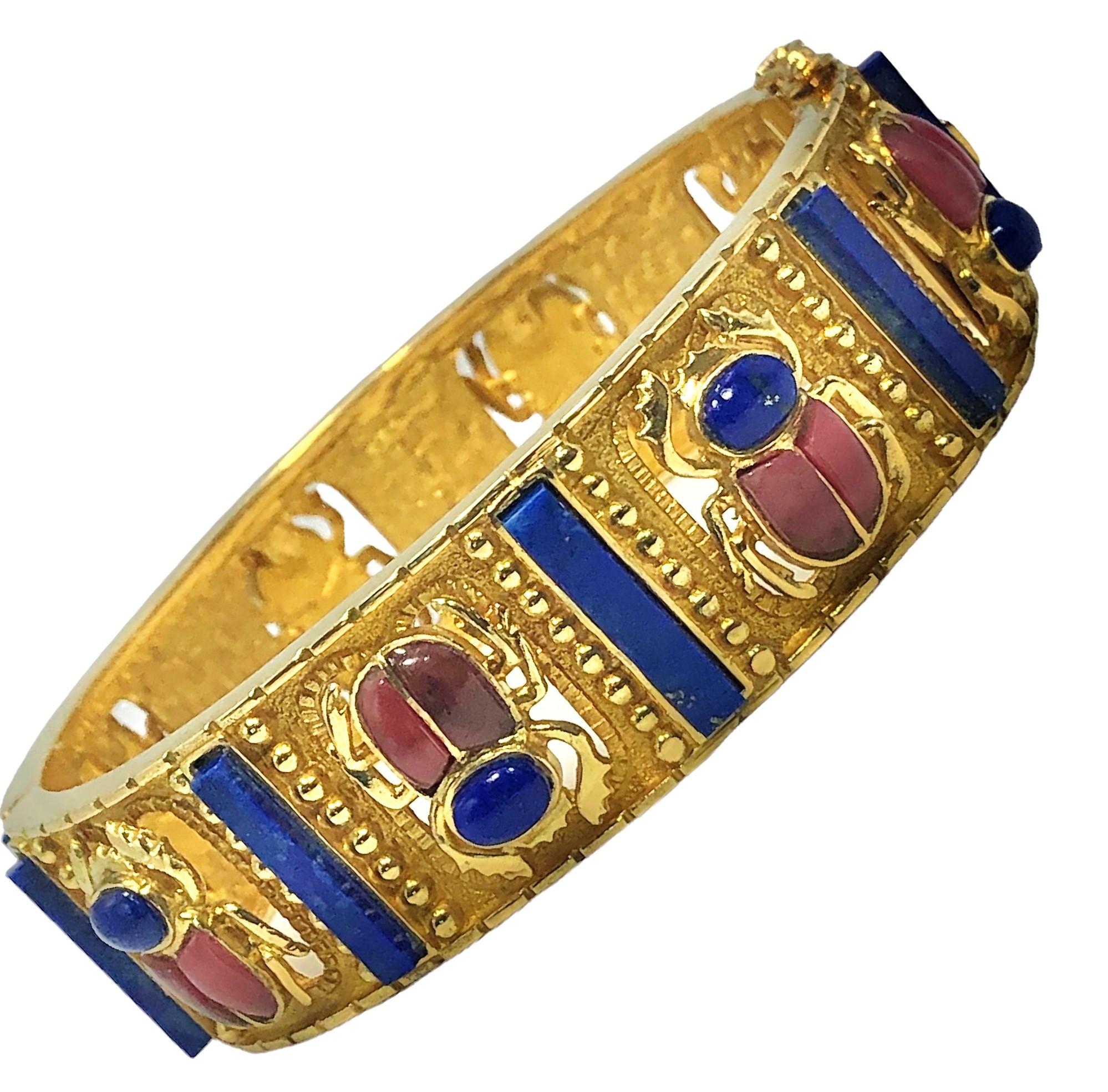 Ce bracelet bangle de style égyptien très bien réalisé présente de nombreuses textures d'or différentes incrustées de colonnes de Lapis Lazuli bleu vif et de huit motifs de scarabées en Lapis et Rhodonite. Charnière sur un côté pour faciliter