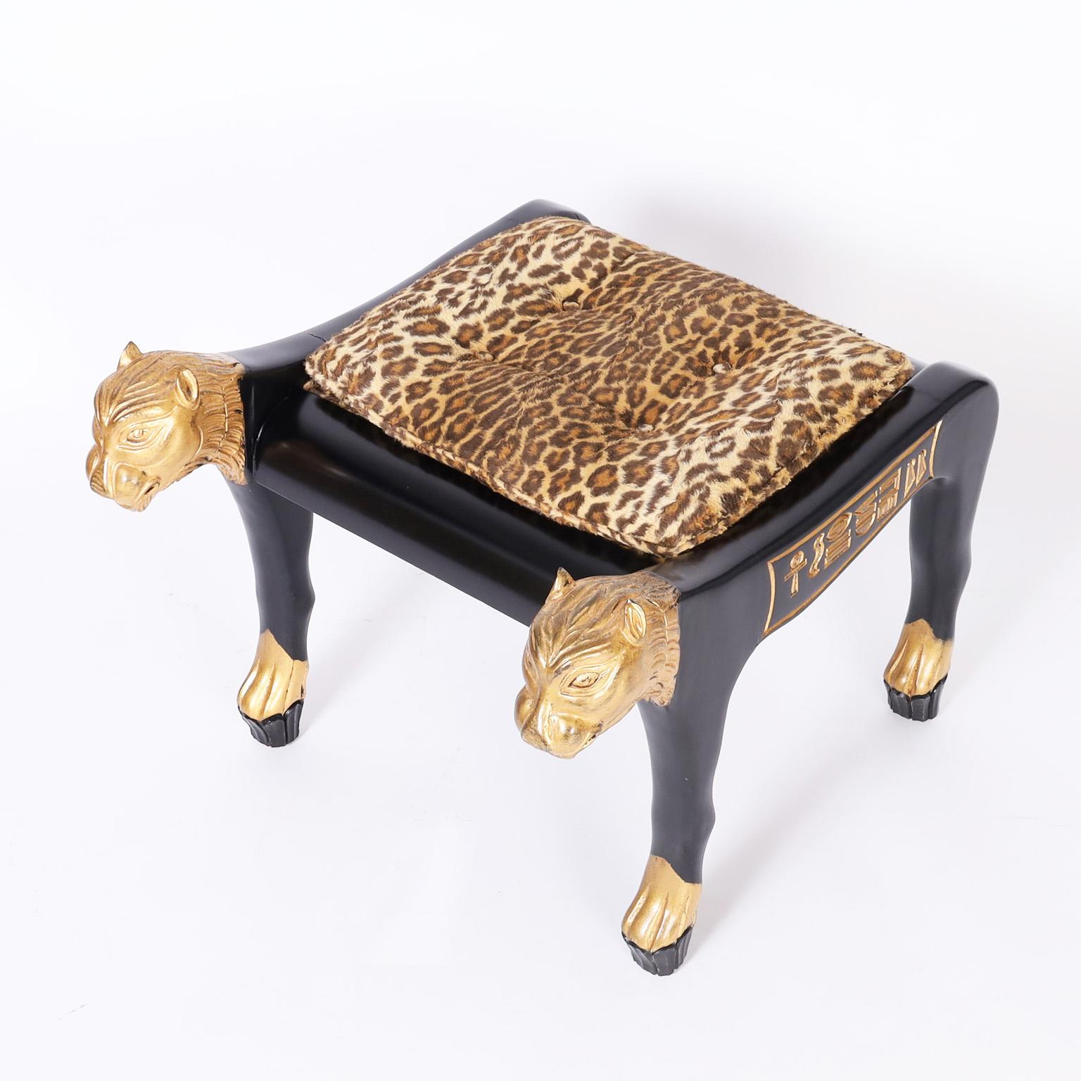 Egyptian style bench featuring button tufted upholstery in faux leopard over an ebonized carved wood base with gilt cat heads, feet, and hieroglyphics.