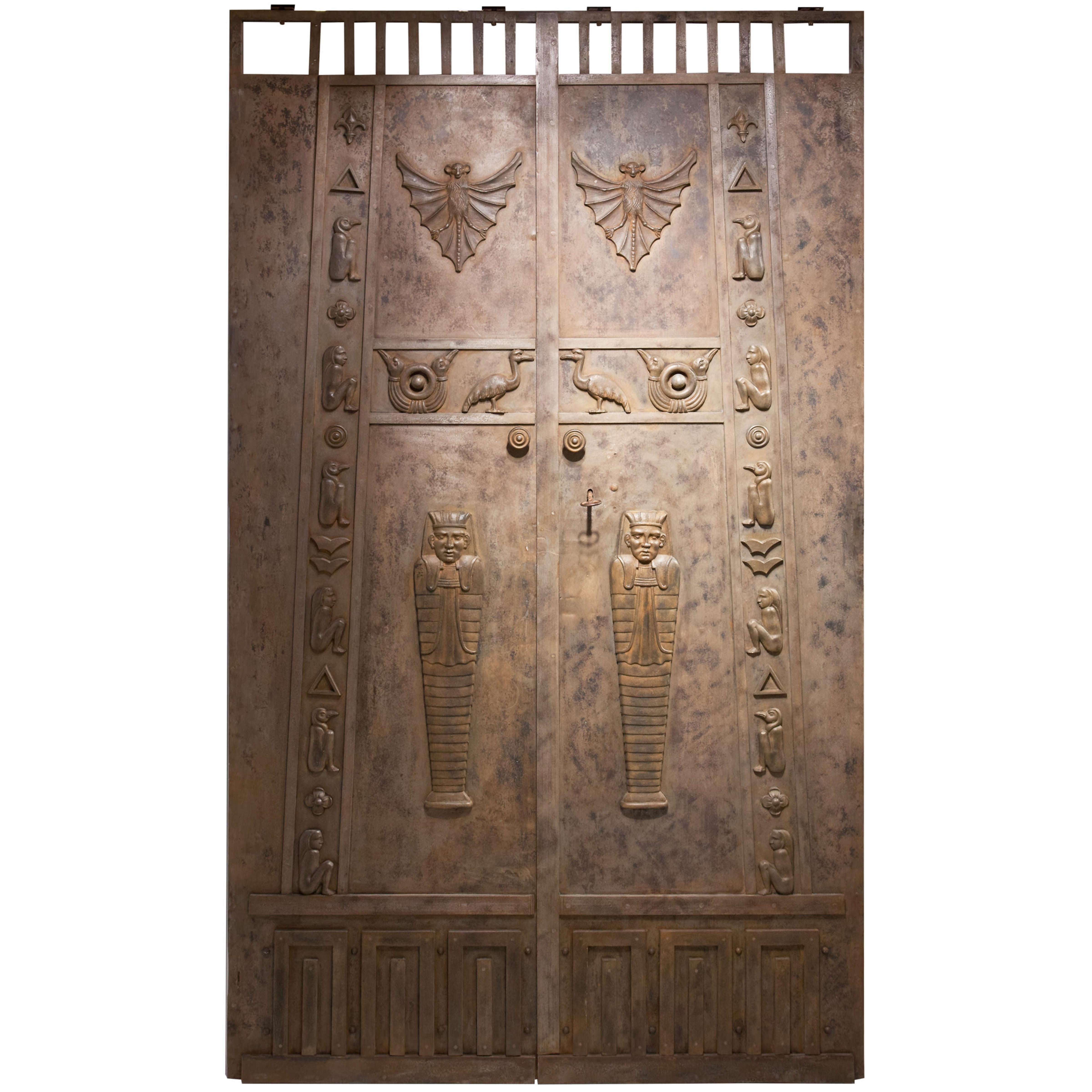 The doors are designed according to an Egyptian pylon. Stylized palace facades at the bottom, slits at the top for ventilation. On the sides geniuses as guardians in the form of falcons and squatting human figures. On the door front bats and sun