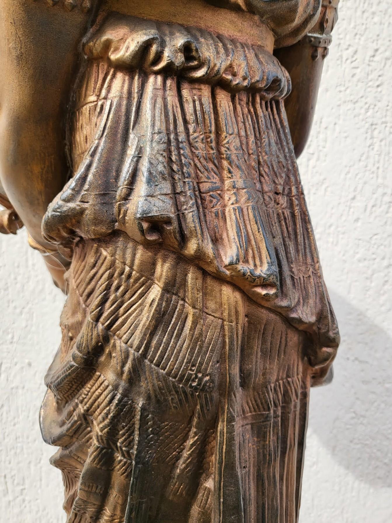Grand sujet en terre cuite patinée représentant une femme égyptienne vêtue d'une longue tunique et portant une couronne avec un oiseau, présentant une urne/offrande dans ses mains

Sculpture signée dans les plis de la robe, difficile à déchiffrer,