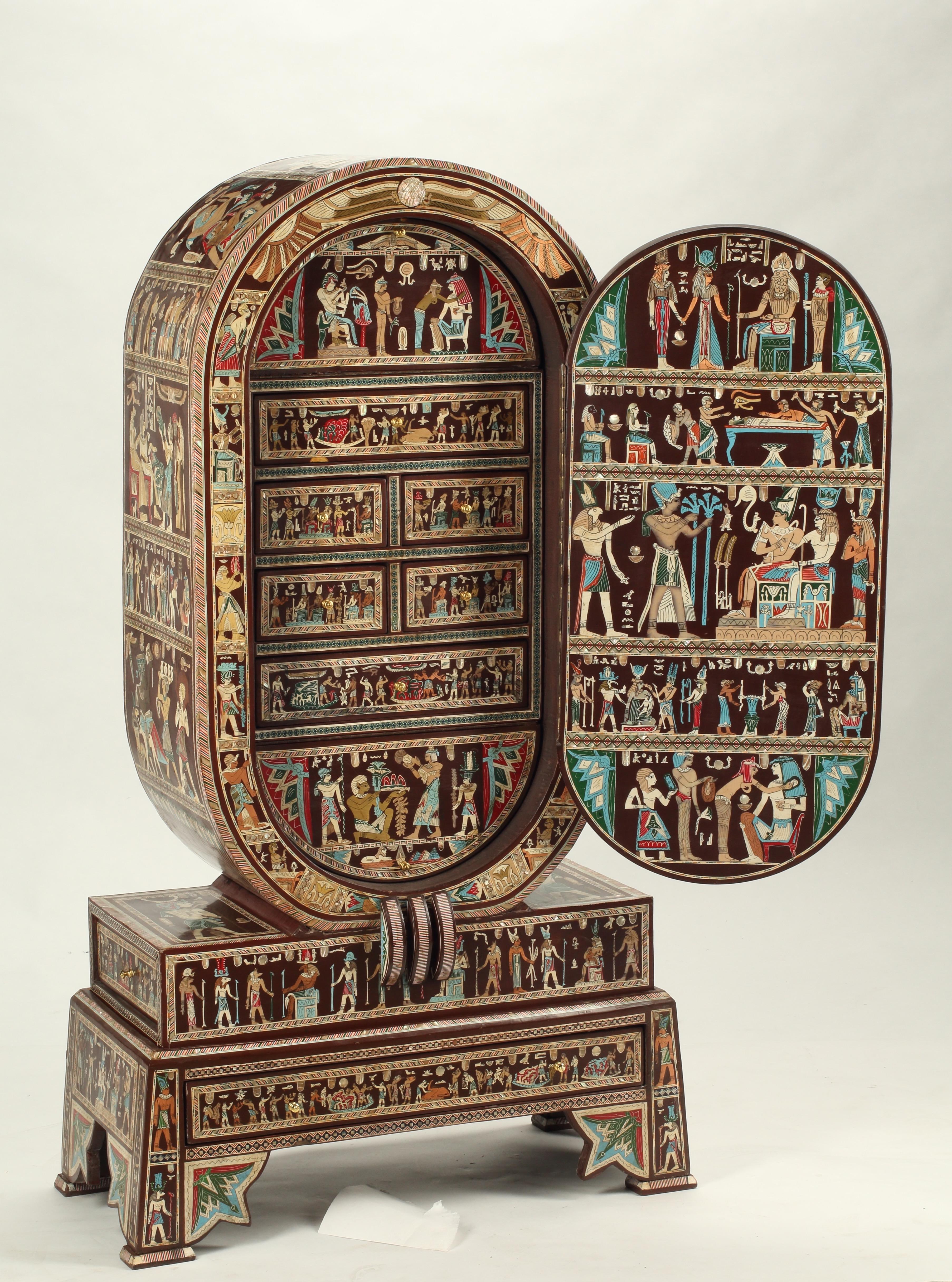 This is a highly unique hand-painted and inlaid Egyptianesque collector's cabinet that pays homage to ancient Egyptian motifs. The cabinet features a rounded top and bottom, and opens to display multiple drawers for treasured collectibles. The
