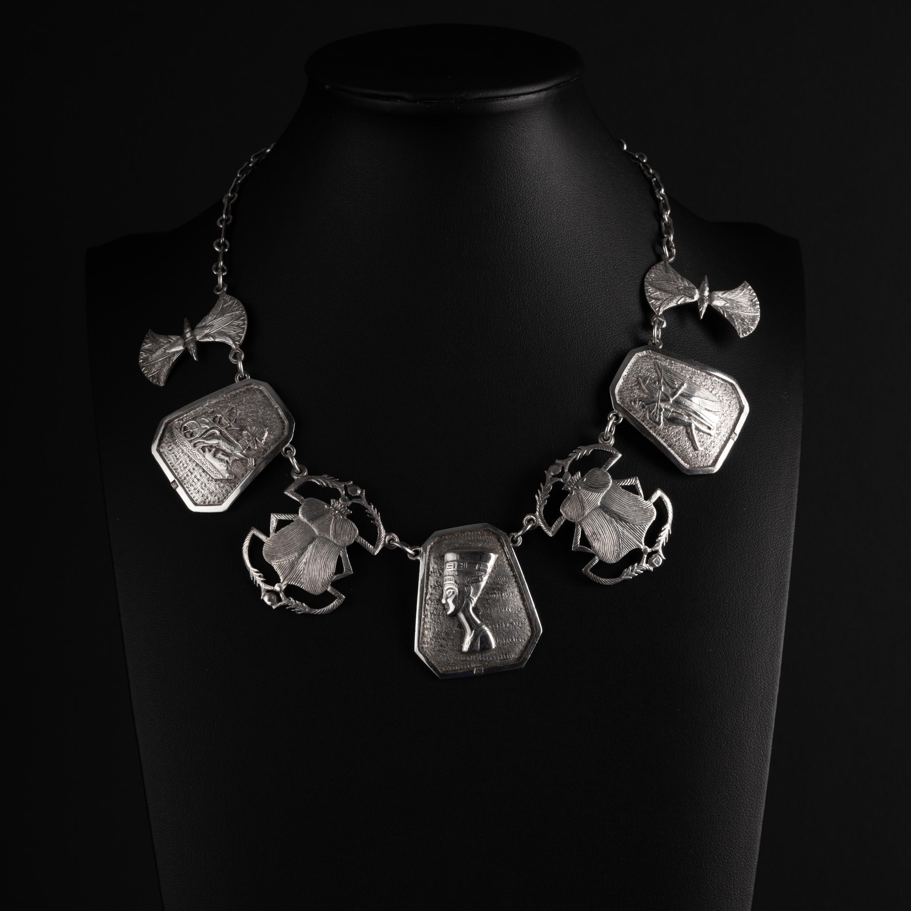This unique, dramatic necklace was created from sterling silver early in the twentieth century —near 1920— at the height of the Egyptian Revival period. The necklace features 7 silver plaques, each of which is highly detailed, depicting war, music,