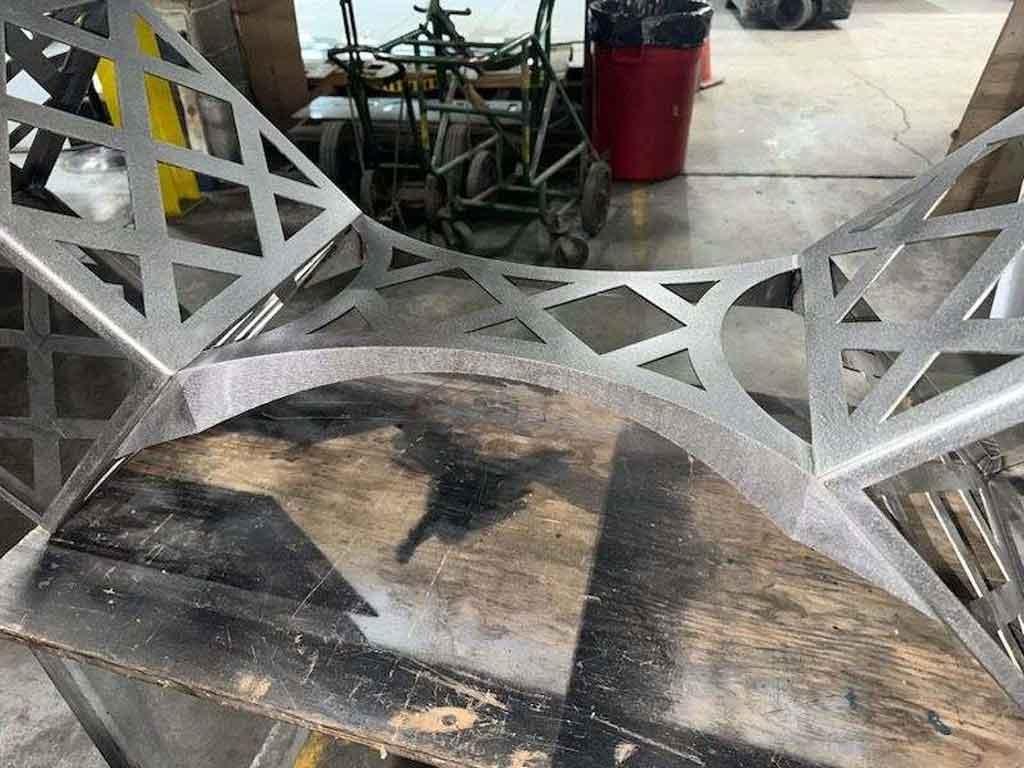 This elegant and functional table is made from laser cut steel and can be powder coated in any color.  The tabletop has the option to be rectangular and can be lucite as well as glass.  The base would also be stunning in stainless steel.  

Size can