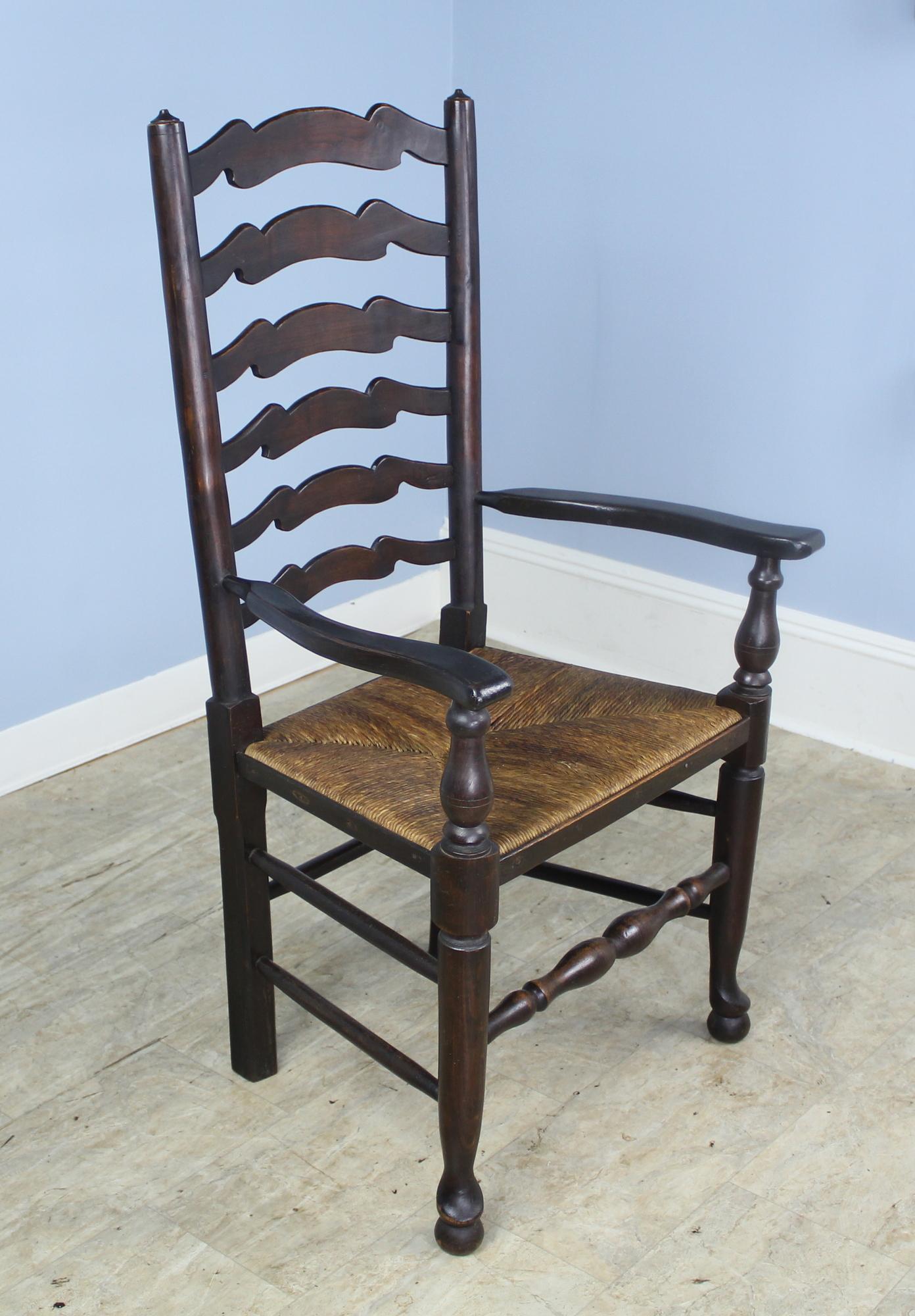 An elegant country look. Set of one arm and seven side English wavy back ladder chairs in dark oak. The rush is in good antique condition, and the chairs are quite comfortable as the backs have a slight recline. A marriage of two sets, these chairs