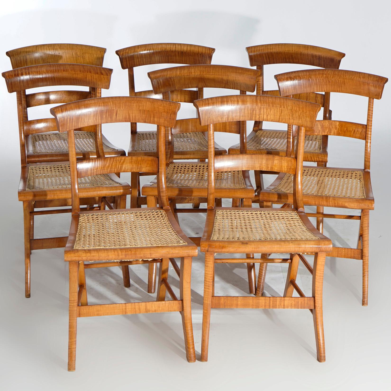 A set of eight antique Federal dining chairs offer tiger maple construction with stylized scroll form rail over slat back, caned seats and splay legs, c1830.

Measures- 33.5''H x 17.5''W x 20''D.