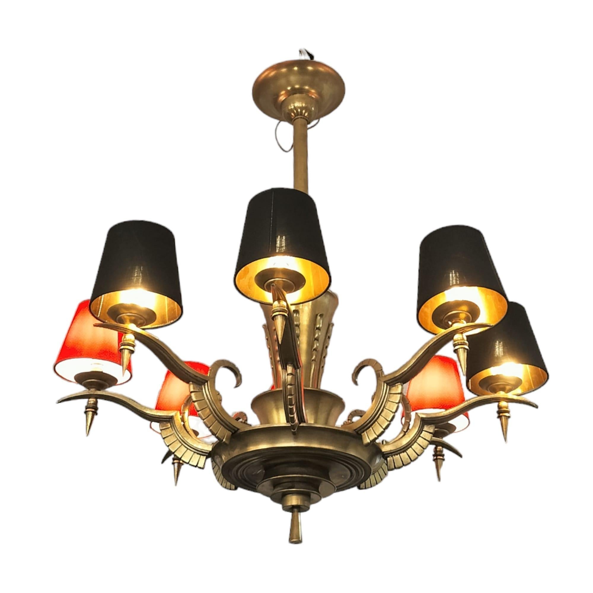 We present you with an early 20th century art-deco chandelier with eight arms, each adorned with feathered crest motifs, crafted in gilded bronze. 

This piece has been modified by replacing the lampshades. We provide two lampshade colour options,