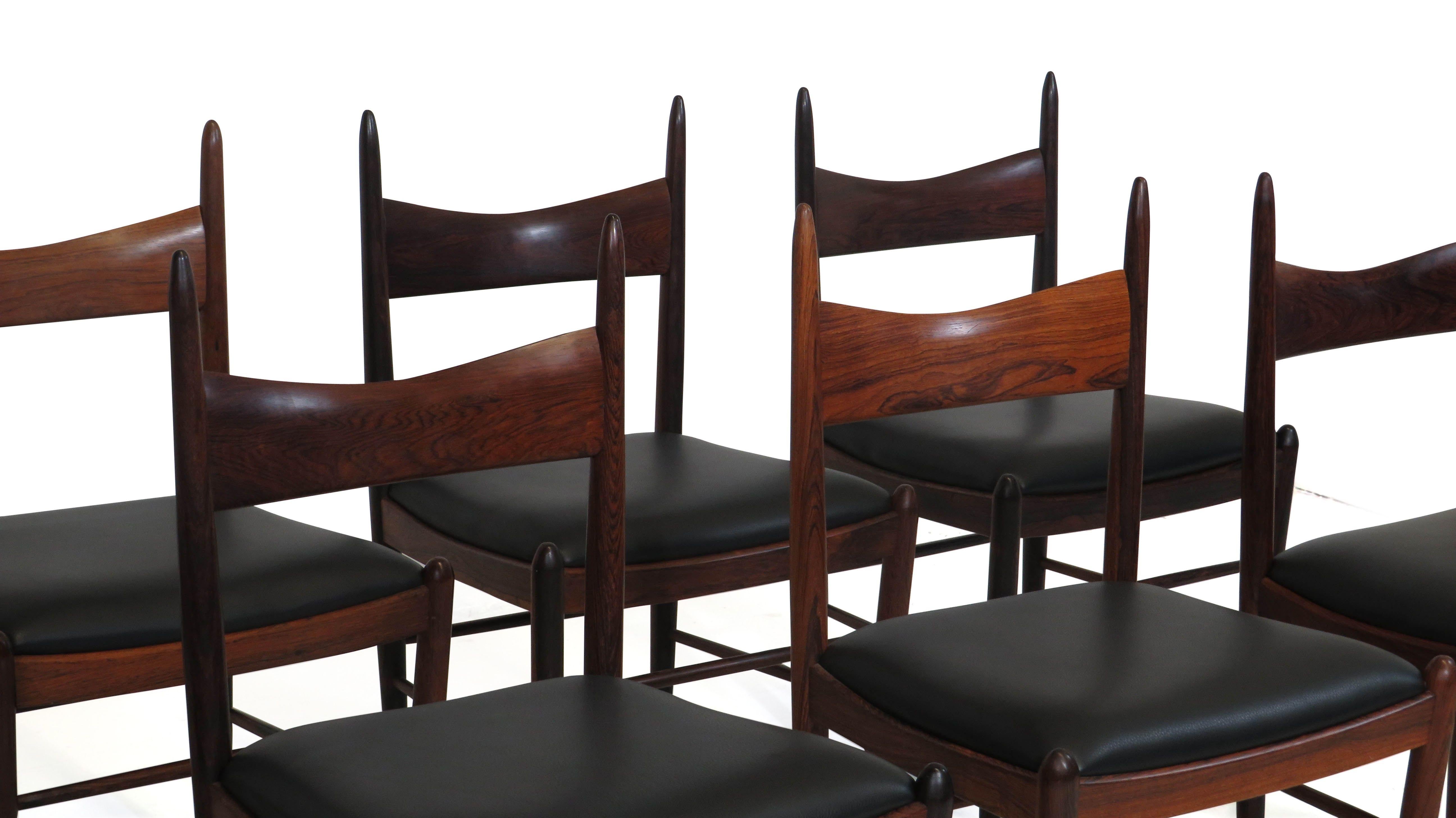 Stunning set of 8 dining chairs handcrafted of solid Brazilian rosewood with sculpted backs and turned legs; newly upholstered in fine black leather. Strong construction and sturdy. These chairs have been fully restored and in excellent condition.