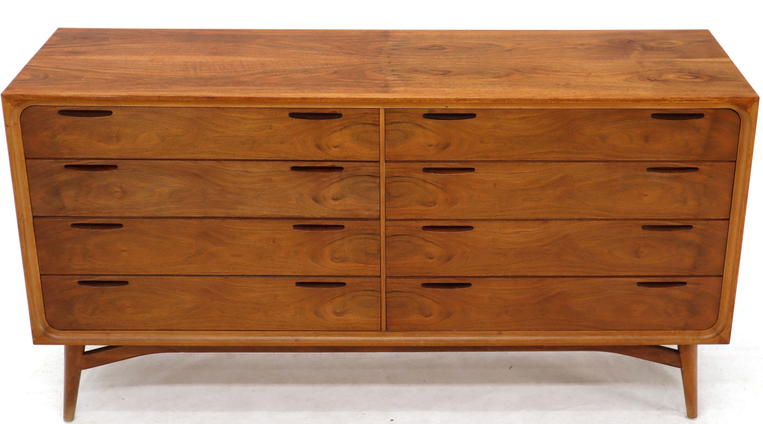 Danish or Swedish Mid-Century Modern 8 drawers double dresser credenza on tall tempered legs and finished back. Dramatic flame walnut wood grain pattern. Banana shape recessed pulls carved into solid walnut. In style of Edmund Spence and Kofoed