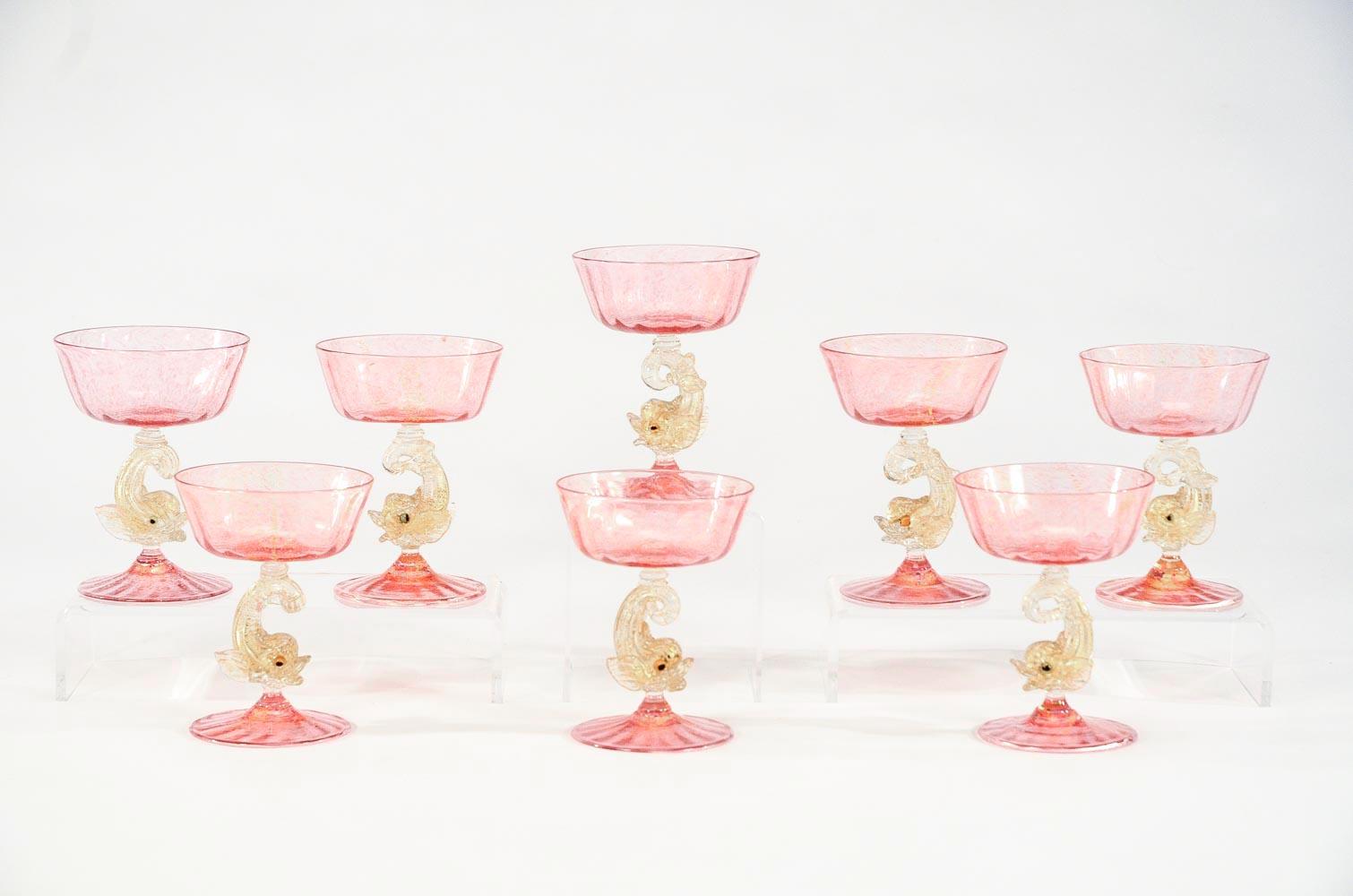 Ready for the season of celebration, this set of eight handblown champagne coupes are sure to enhance any occasion. Made by Salviati, these feature rose pink optic rib bowl and foot with gold leaf inclusions and topped off with full figural dolphin