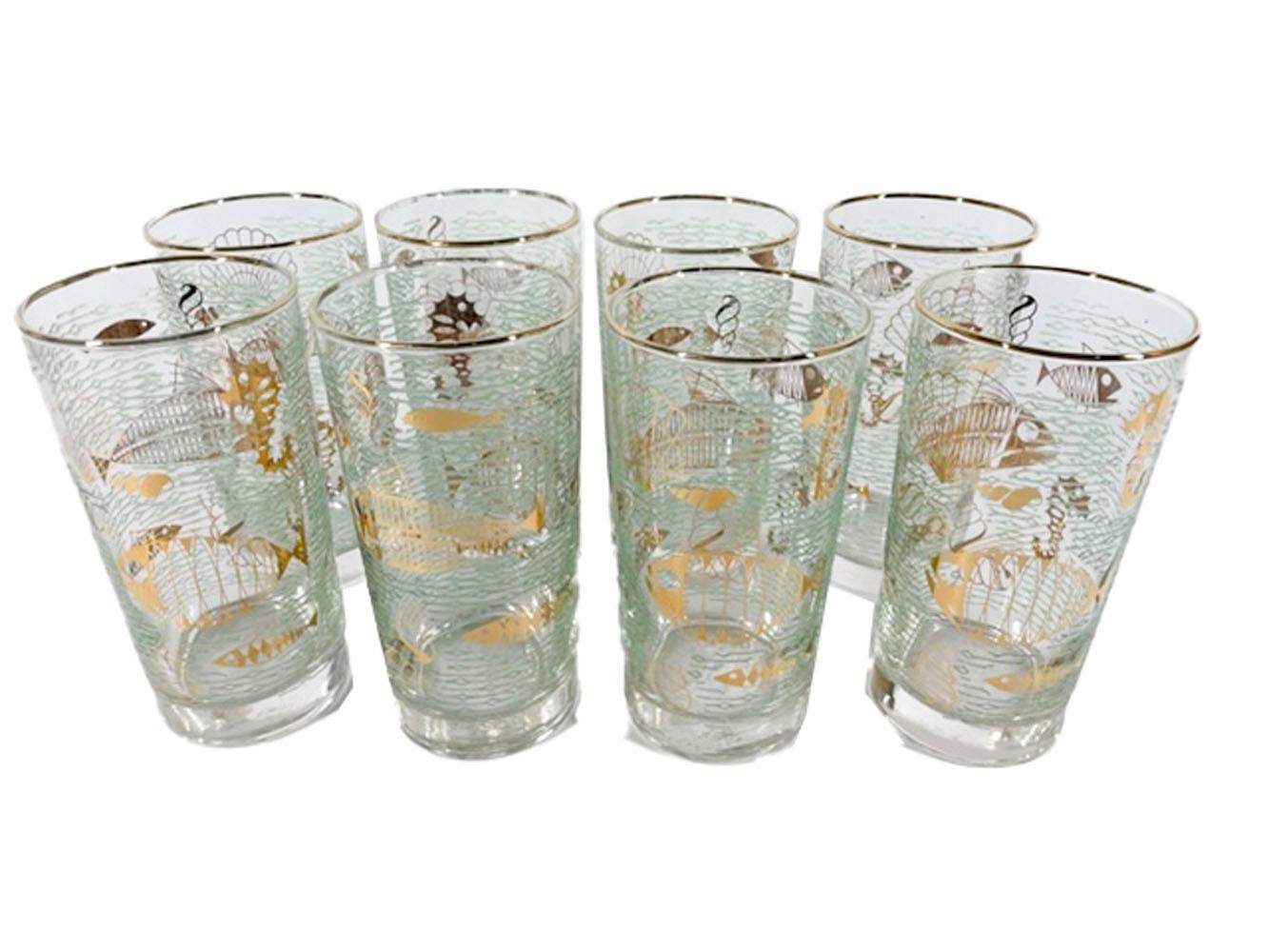 Eight Mid-Century Modern highball glasses by Libbey in the Atomic period Marine Life pattern with stylized fish in 22k gold against a ground of raised green translucent waves. This set comes with a gold-tone wirework caddy.
