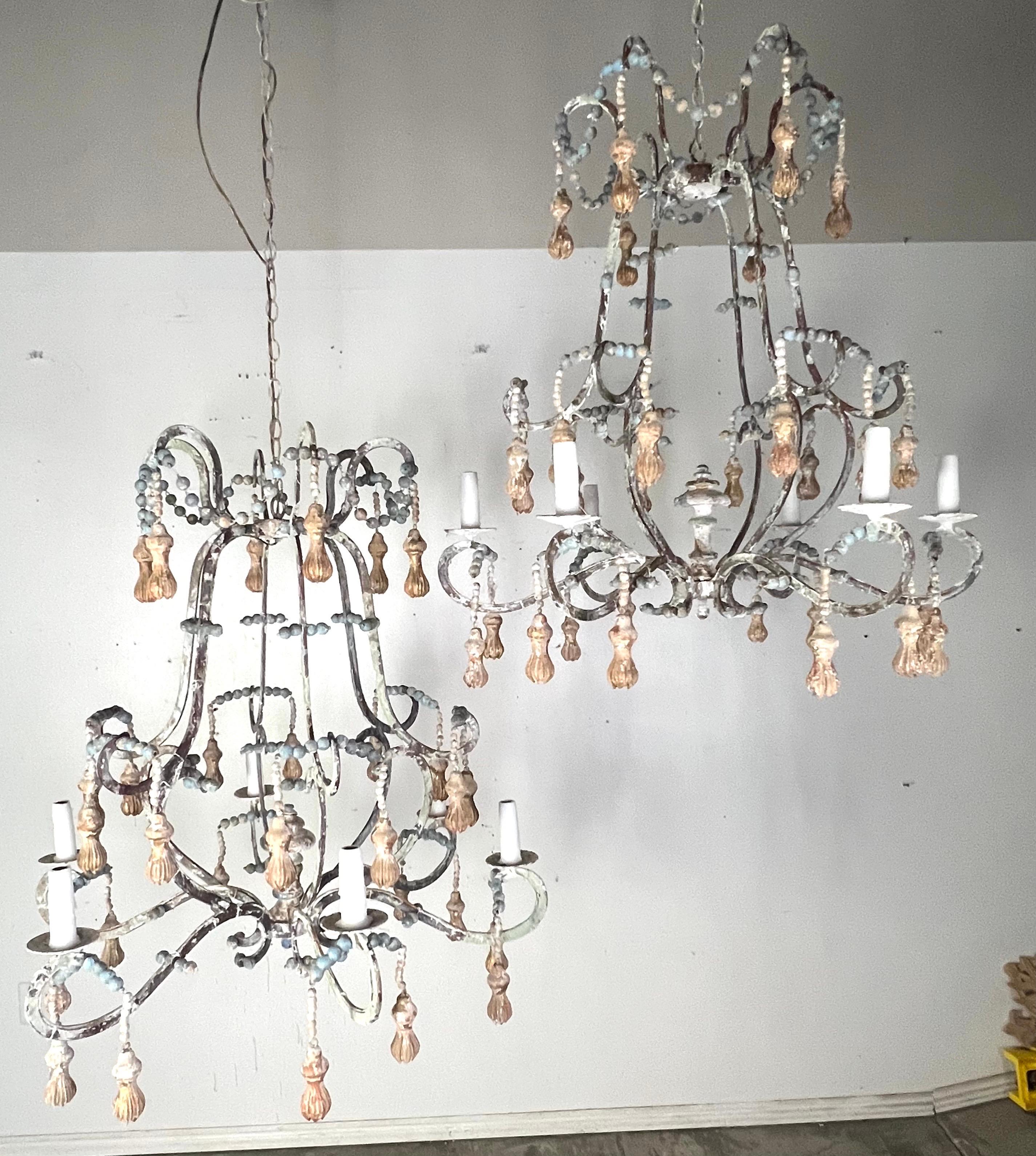 Hand crafted wood beaded and iron painted chandelier.  The chandelier has a distressed appearance with an iron frame featuring the same aged appearance, a mix of oxidized green and rusted brown tones.  It is adorned with decorative elements such as
