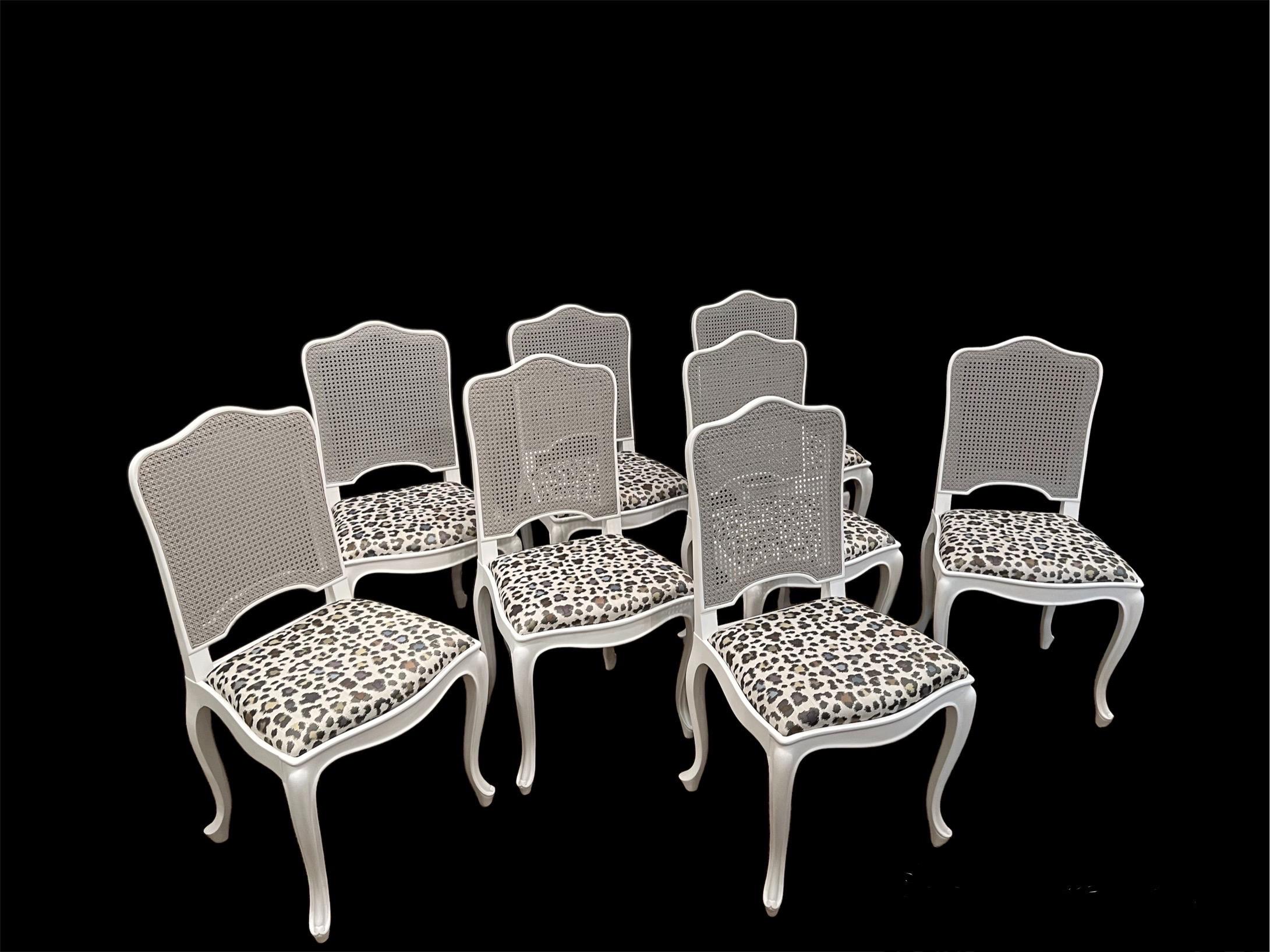 Huit chaises de salle à manger de style Louis XV à dossier en rotin et sièges en tissu. Les cadres des chaises sont finement peints en blanc mat et les dossiers sont peints dans un gris pâle doux. Les cadres des chaises sont serrés et les sièges ont