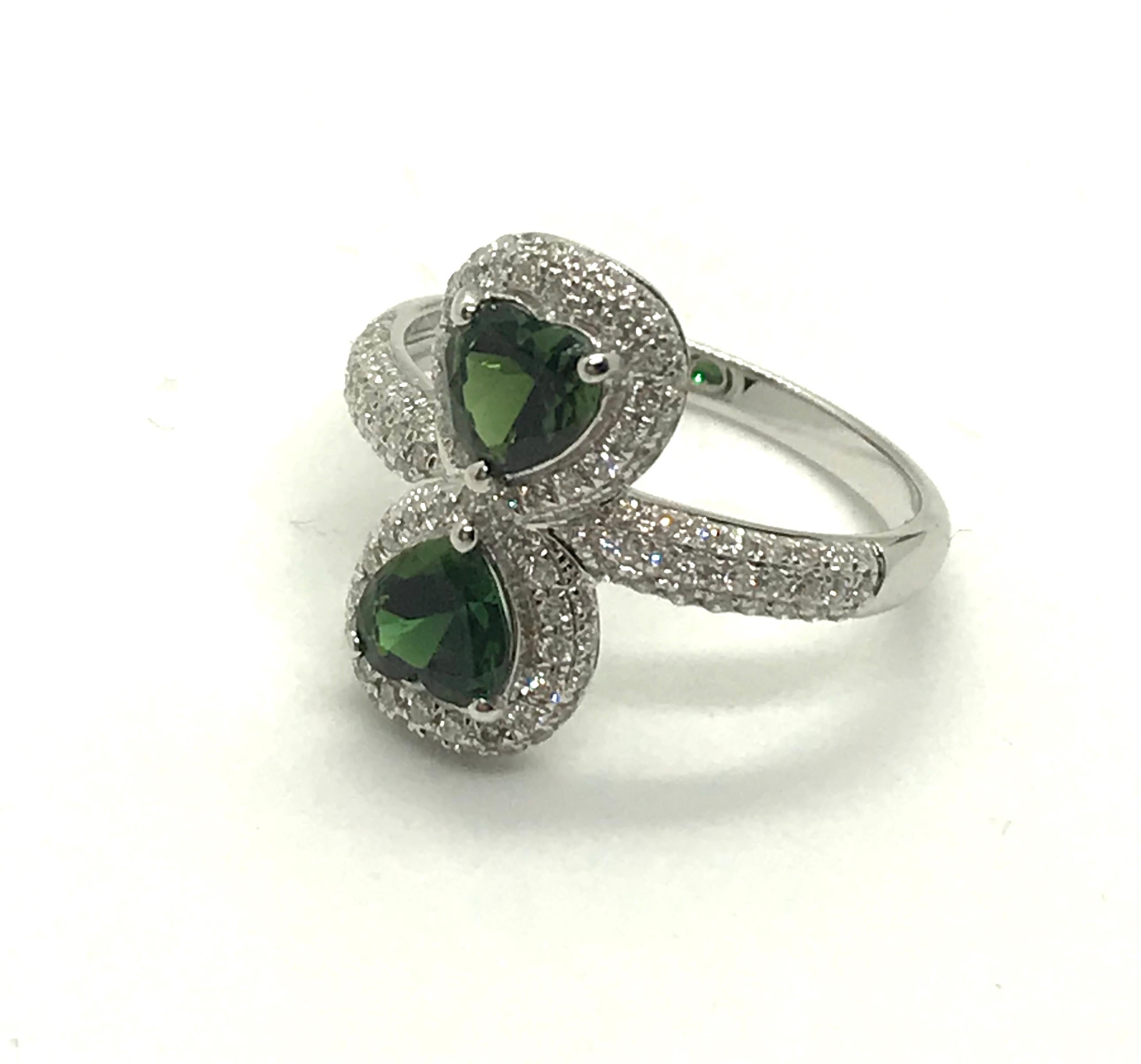 A 18K white gold, diamonds (0,454 ct) and heart-shaped green tourmalines (0,91ct) ring.Size 53.
“Eight of hearts” diamonds and colored stones rings offer a double symbol : number eight brings prosperity and luck, while the two hearts symbolize love
