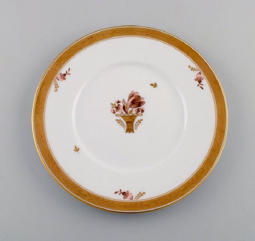 Eight Royal Copenhagen golden basket plates in porcelain with flowers and gold decoration. 
Model number 595/10520.
Diameter: 23 cm.
In excellent condition.
Stamped.