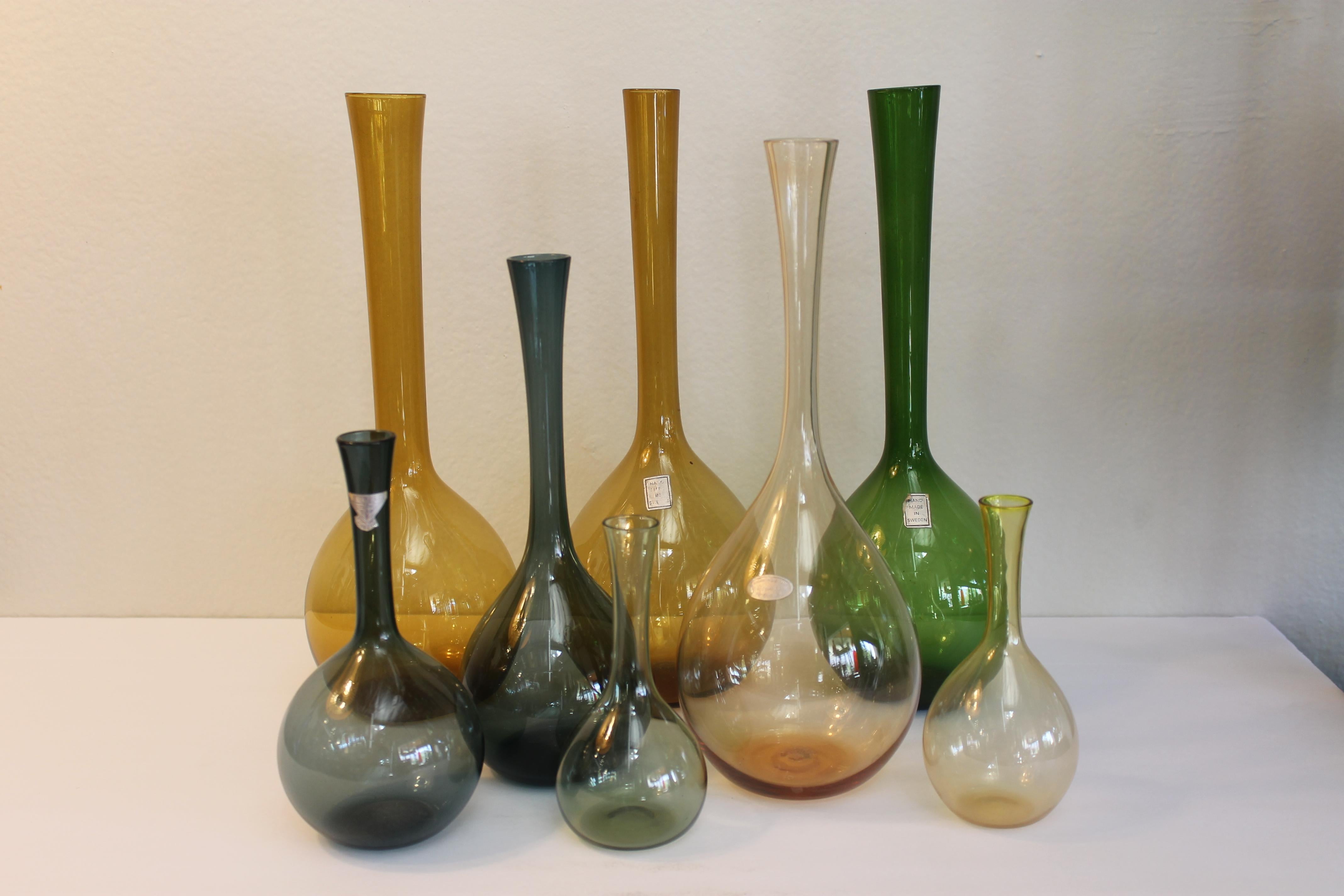 Huit bouteilles en verre fabriquées en Suède par Arthur Percy en vert, bleu et ambre. Les tailles vont de 5,25