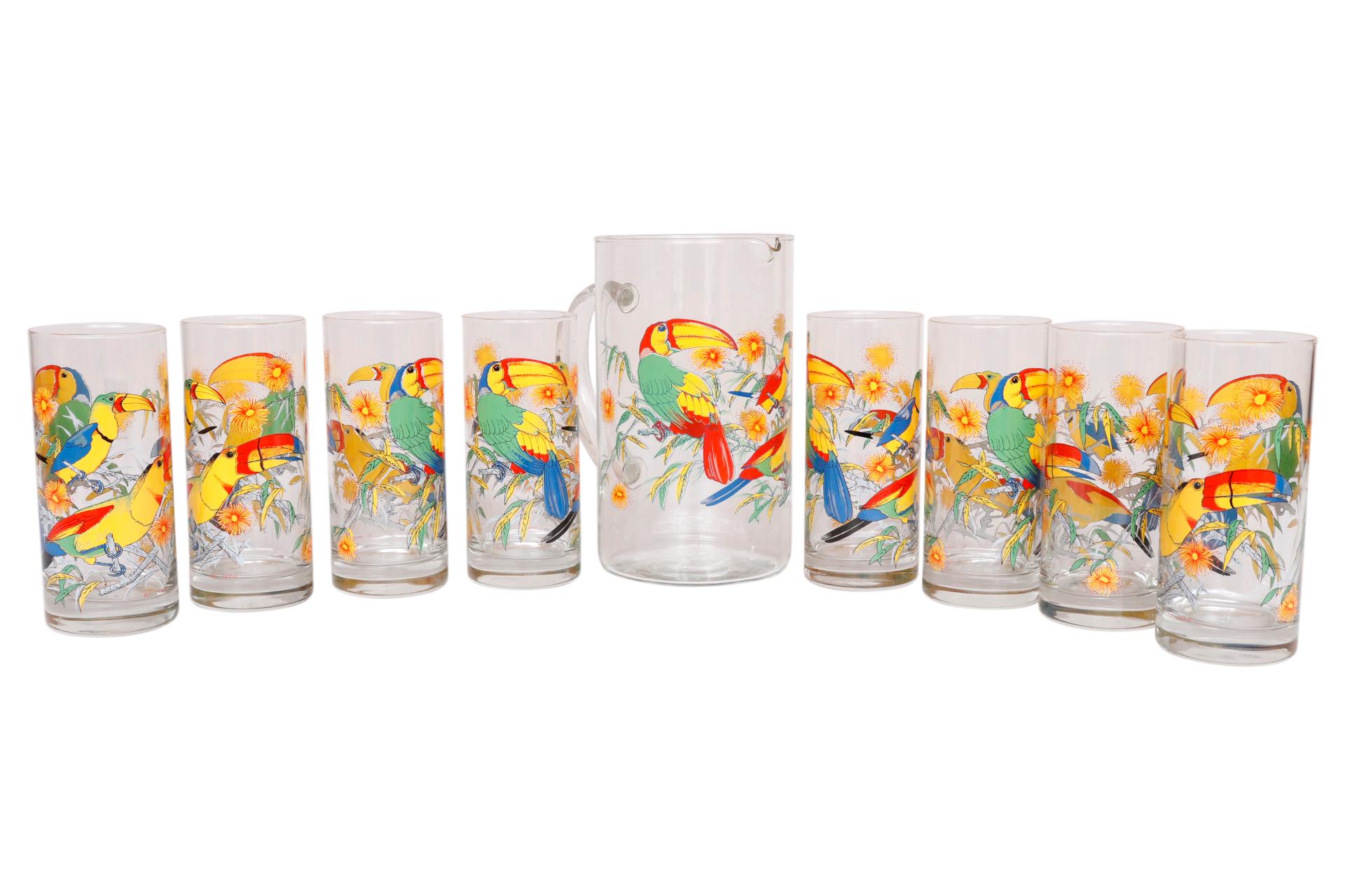 A set of eight glass tumblers with matching glass pitcher. Glasses are printed with colorful toucans and bright yellow flowers. The pitcher has a narrow spout for pouring and a clear glass handle. Made in Italy by Cerve. Each glass measures 2.5