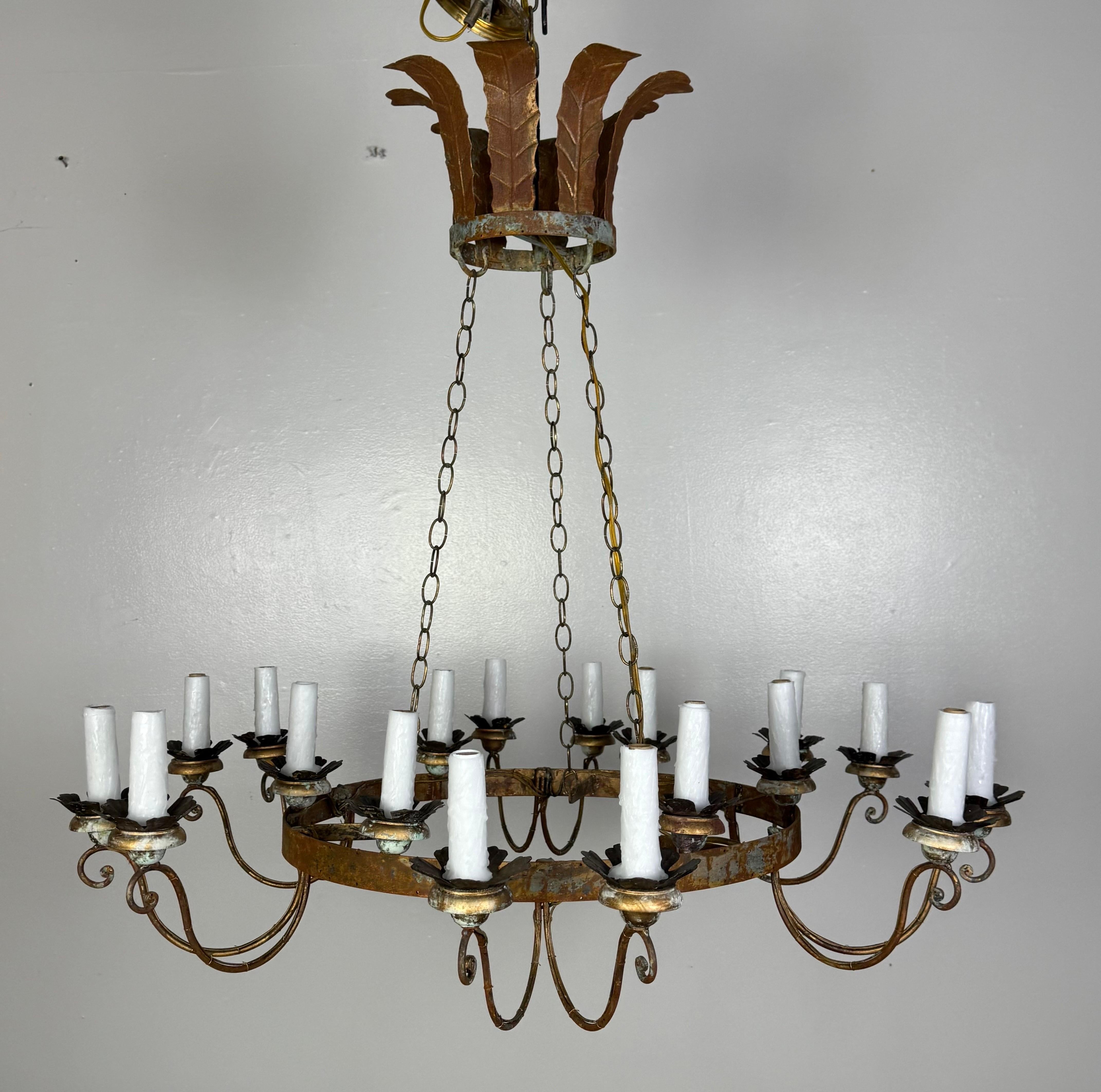 This stunning Spanish-style 18-light chandelier is a striking example of old-world craftsmanship and ornate Mediterranean design. It features a circular wrought iron frame with a rustic patina, showcasing intentional aging and oxidation that