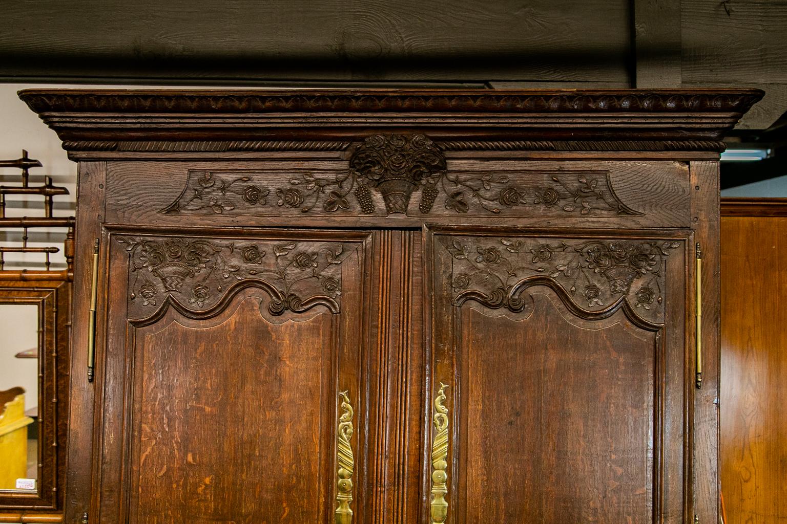 18th century carved Oak French armoire has the original brass escutcheons and hinges. The cornice is carved with interlaced acanthus leaves and gadrooned molding. The frieze has a carved basket of flowers and grapes. The doors are carved with