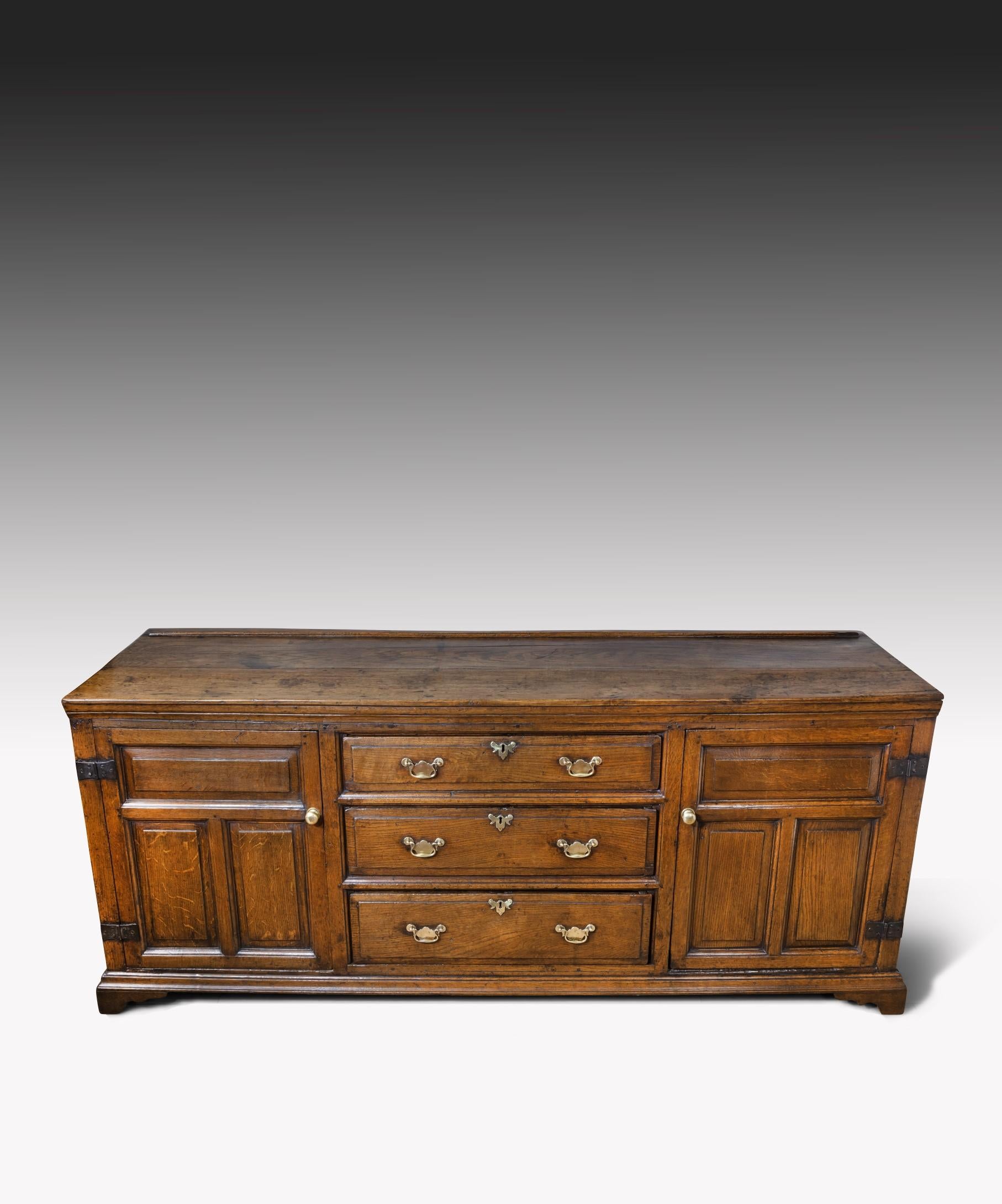 An 18th century Georgian oak dresser base; the oak dresser has three frieze drawers above a central bank of graduated drawers flanked by a panelled cupboard door to either side and is raised on the original bracket feet. The dresser's drawers have