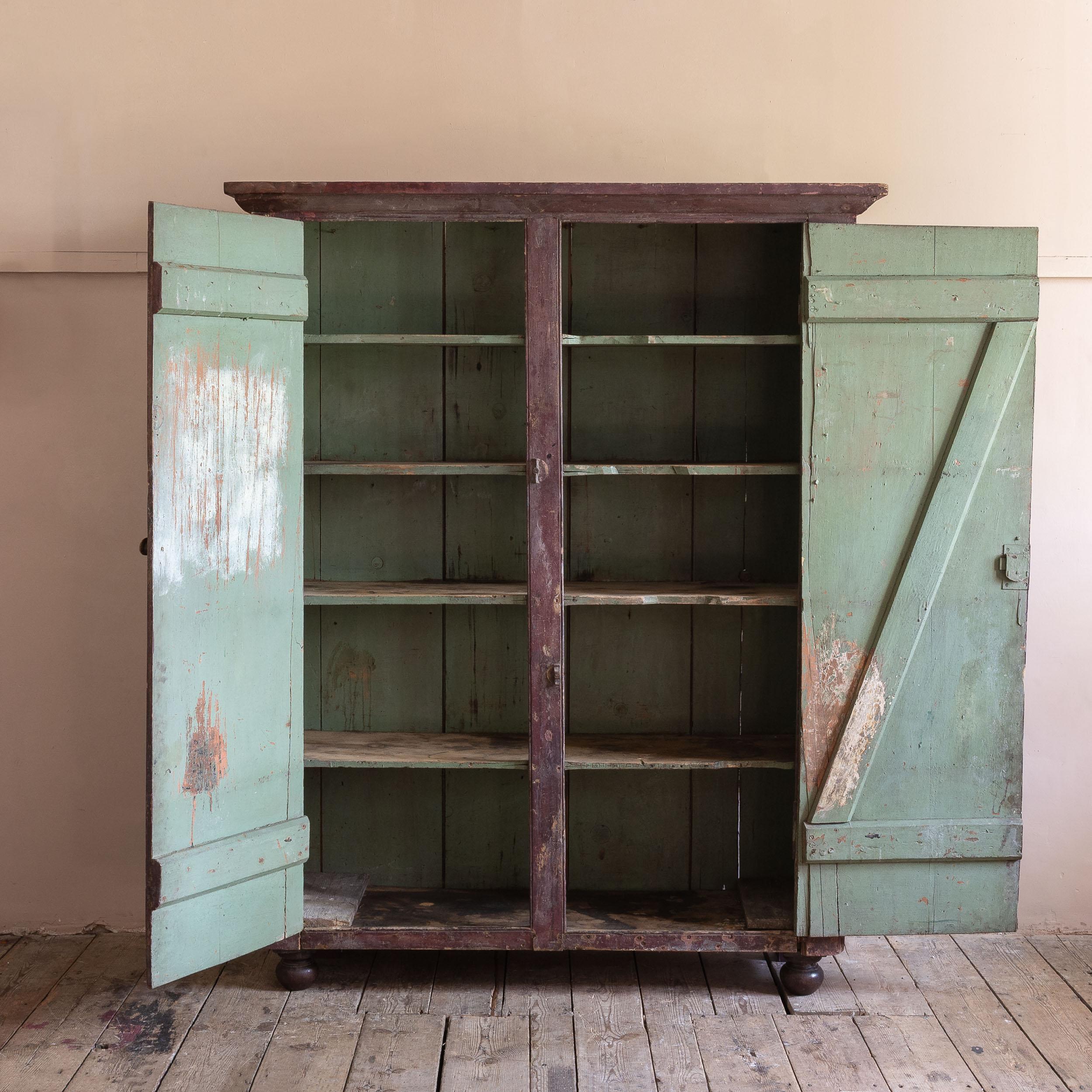 An eighteenth century painted cabinet, the exterior retaining its remarkable historic and patinated paint finish, the cupboard doors with iron strap hinges opening to reveal arsenic green shelved interior, all raised on later turned feet.

