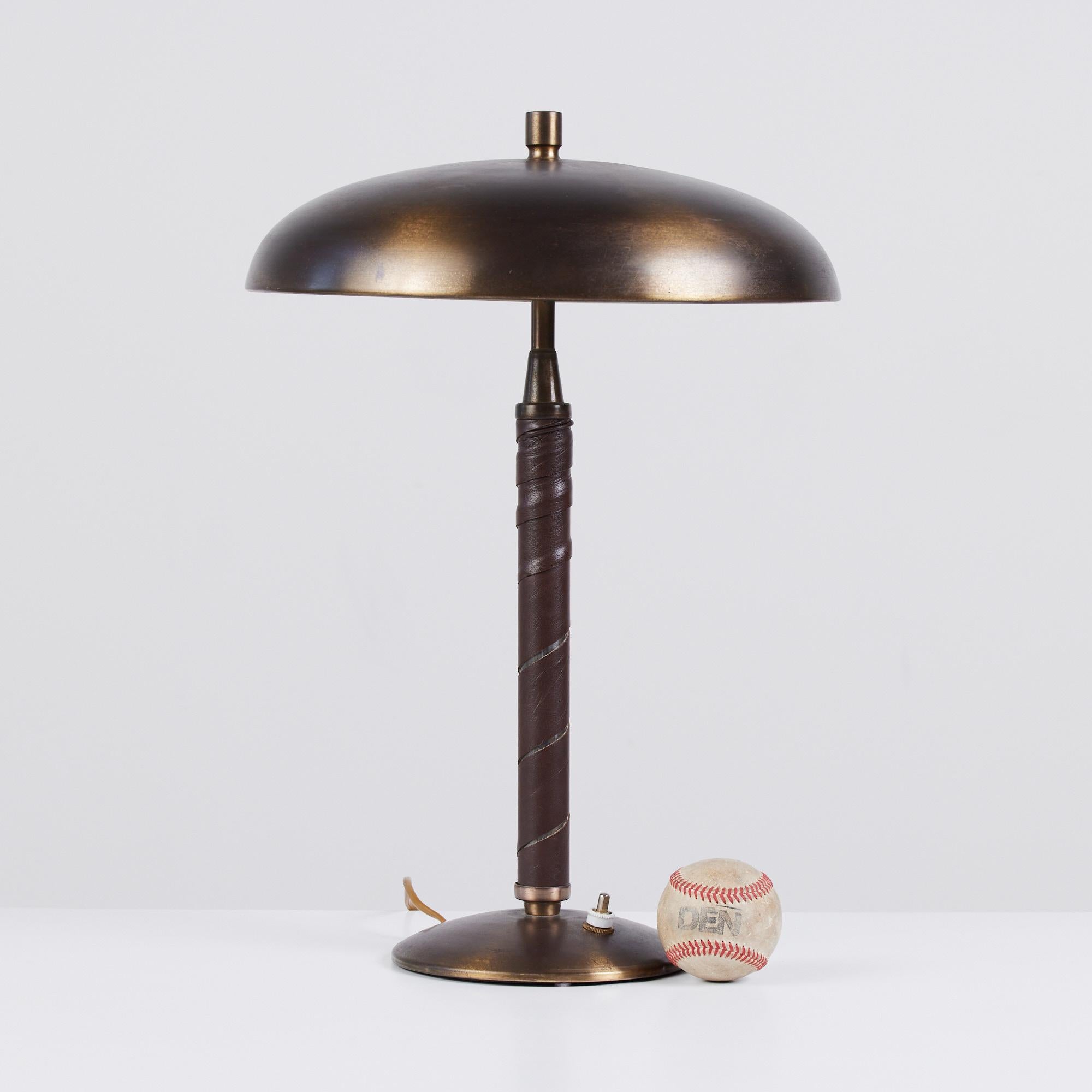 Table lamp by Einar Bäckström c.1950s, Sweden. The lamp features an aged brass stem wrapped in a chocolate brown leather. The brass dome shade is patinated to perfection housing two light bulbs. The round base has a petite on/off switch.

Marked