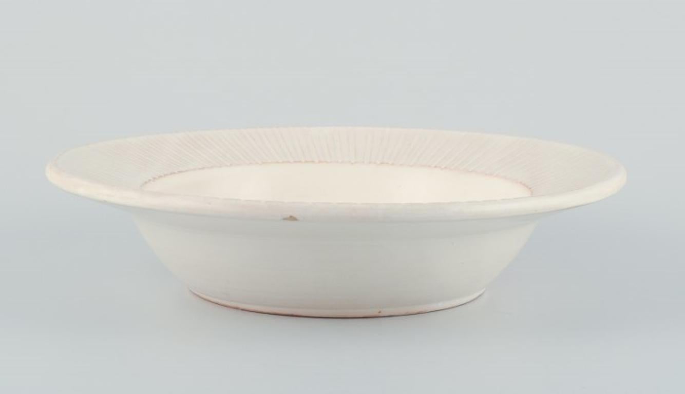 Einar Johansen, Danish ceramist. 
Unique ceramic bowl with a motif of leaping deer. Art Deco style.
Cream-colored glaze.
Approximately from the 1970s.
Signed.
Label from the department store Illum, Copenhagen.
In excellent condition with small chip