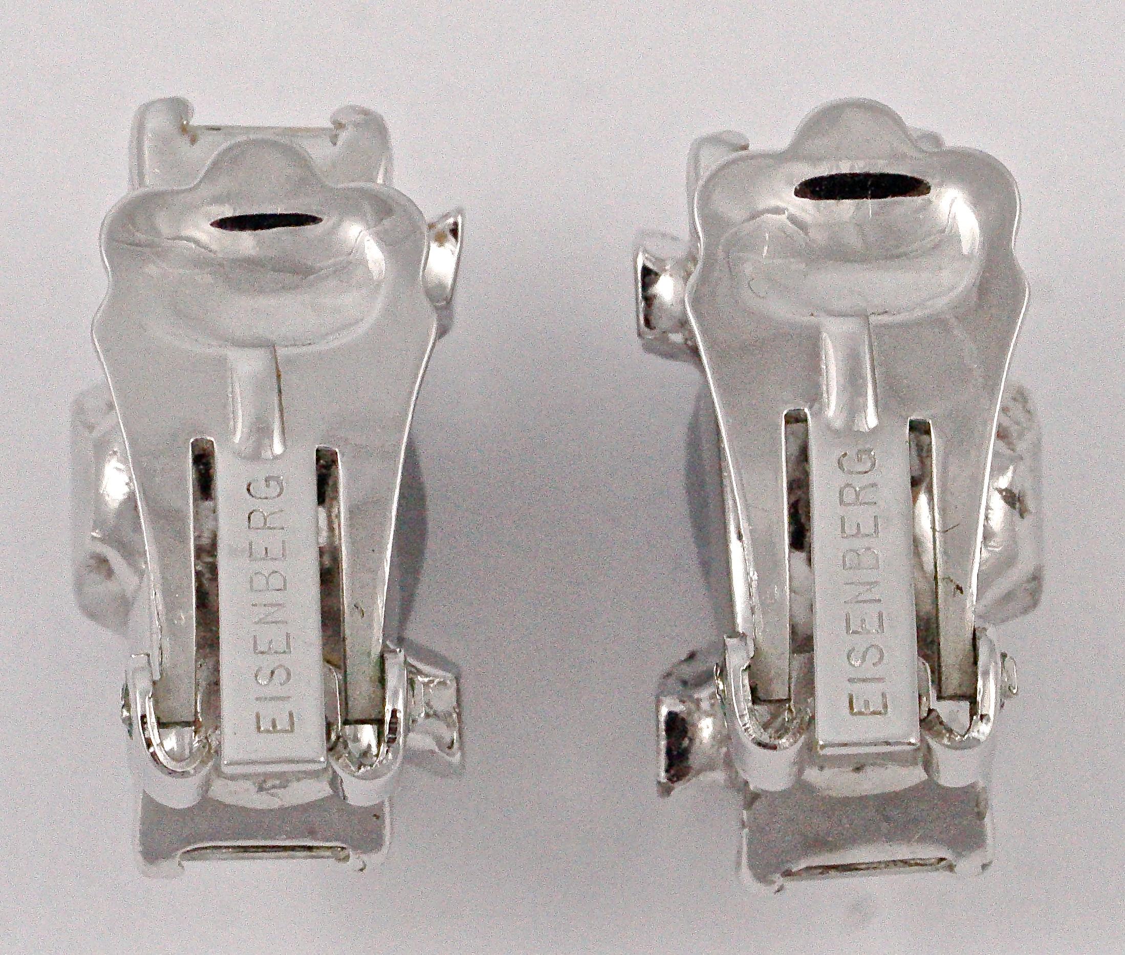 Beautiful Eisenberg silver tone clip on earrings, featuring round and emerald cut clear rhinestones. They have an unusual design with the large emerald cut rhinestones overlaid with an abstract V shape set with round rhinestones. Measuring length