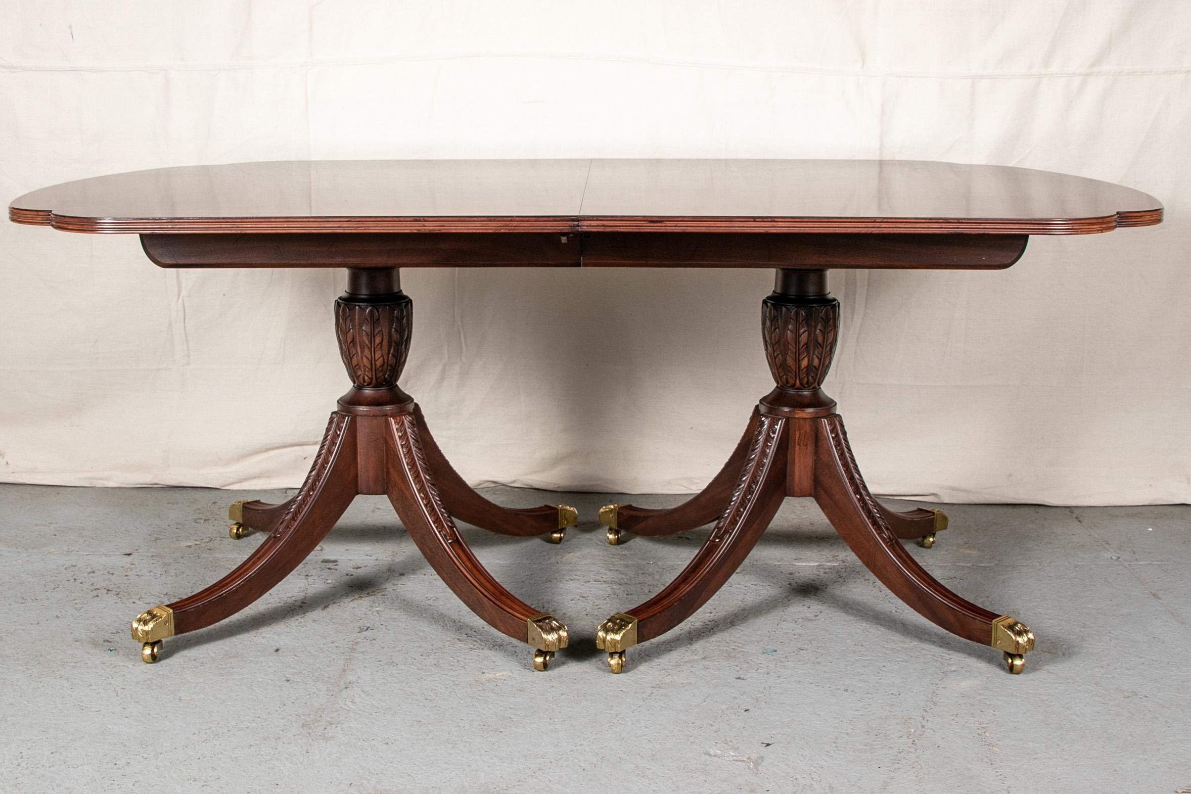 E.J. Victor mahogany dining set with table and 12 chairs, long banded flame mahogany table with curved ends and two carved supports with leafy balusters and four leafy reeded outswept legs. Brass lion's paw caps on casters. Along with three leaves.