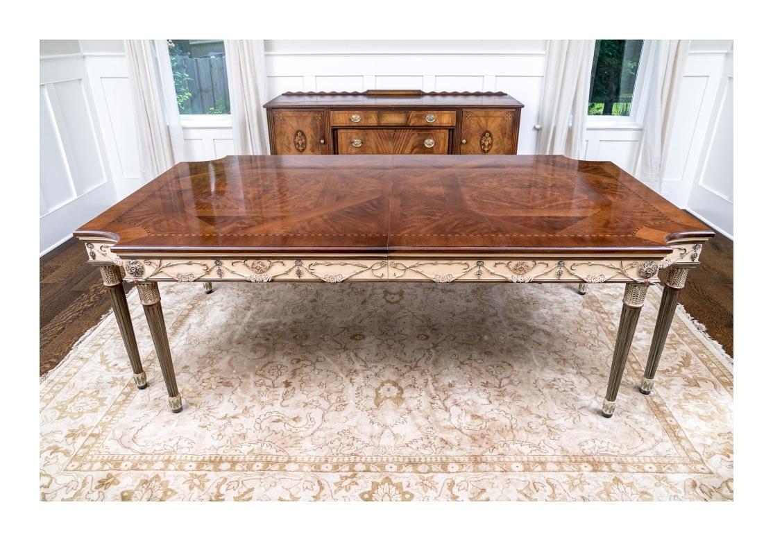 A paint decorated dining table with two leaves that showcases the fine quality of E. J. Victor. Crafted from walnut solids and veneers, the table with unique polychrome floral swag carvings, rich figured parquetry inlaid top and resting upon fluted