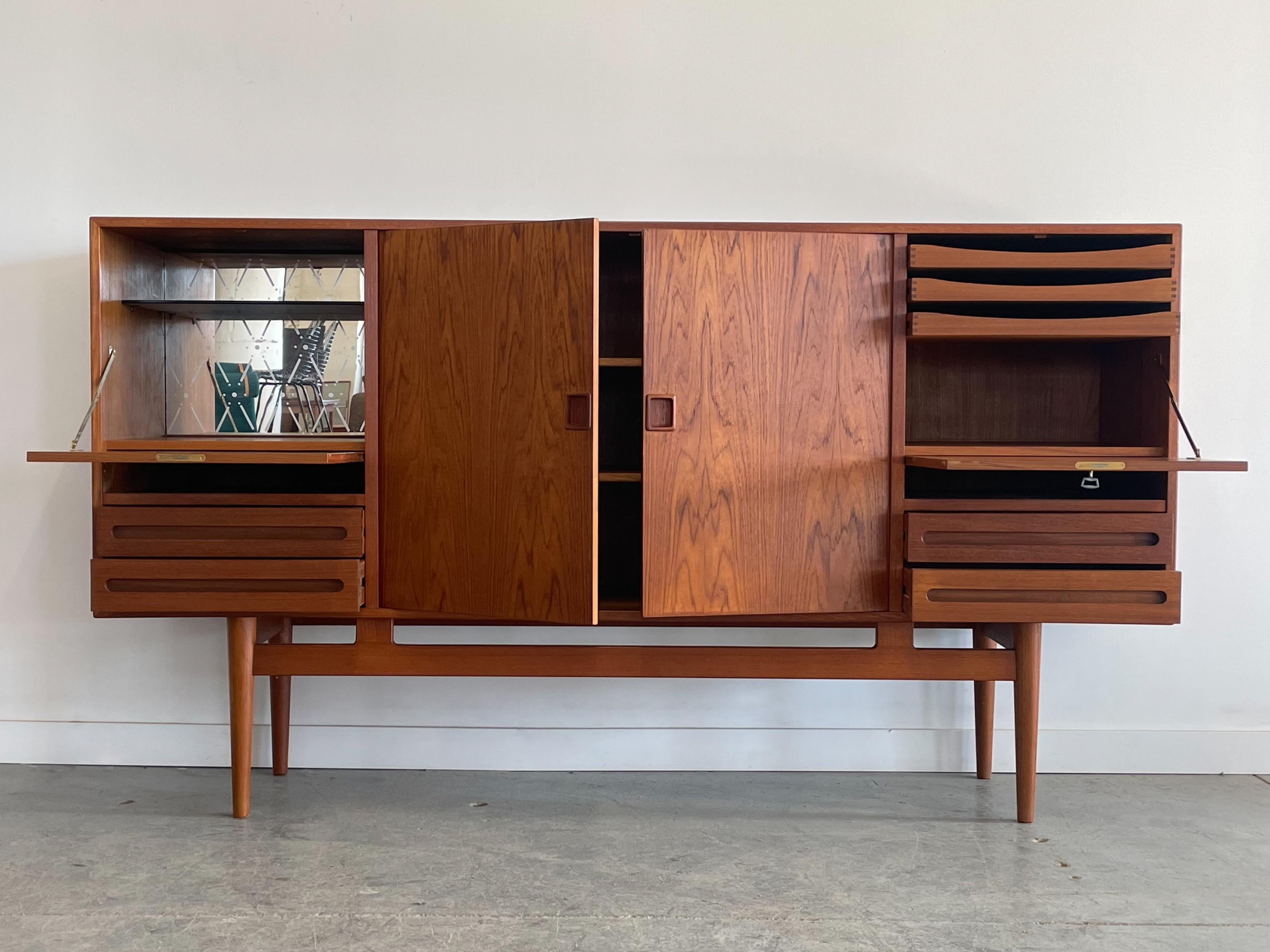 Incredible Danish teak highboard designed by Ejvind Johansson. This piece features solid construction with a rich book-matched grain pattern. It offers a variety of storage options, including internal and external drawers, adjustable shelving, and