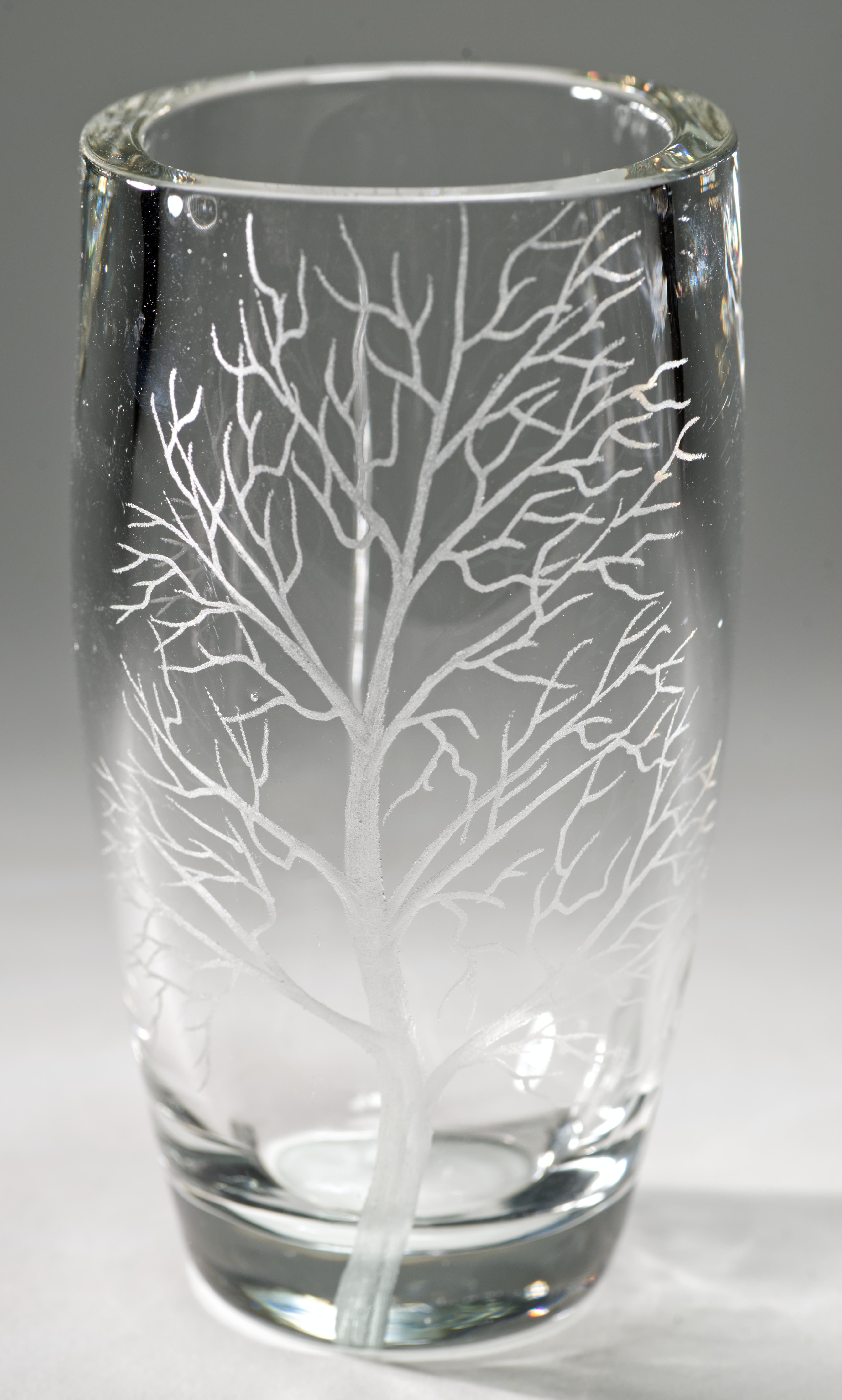 Il vaso di cristallo vintage presenta un decoro modernista inciso che raffigura due persone che si stringono sotto un ombrello sotto i rami spogli di un grande albero. Le decorazioni sono posizionate in modo da enfatizzare la morbida forma ovale del