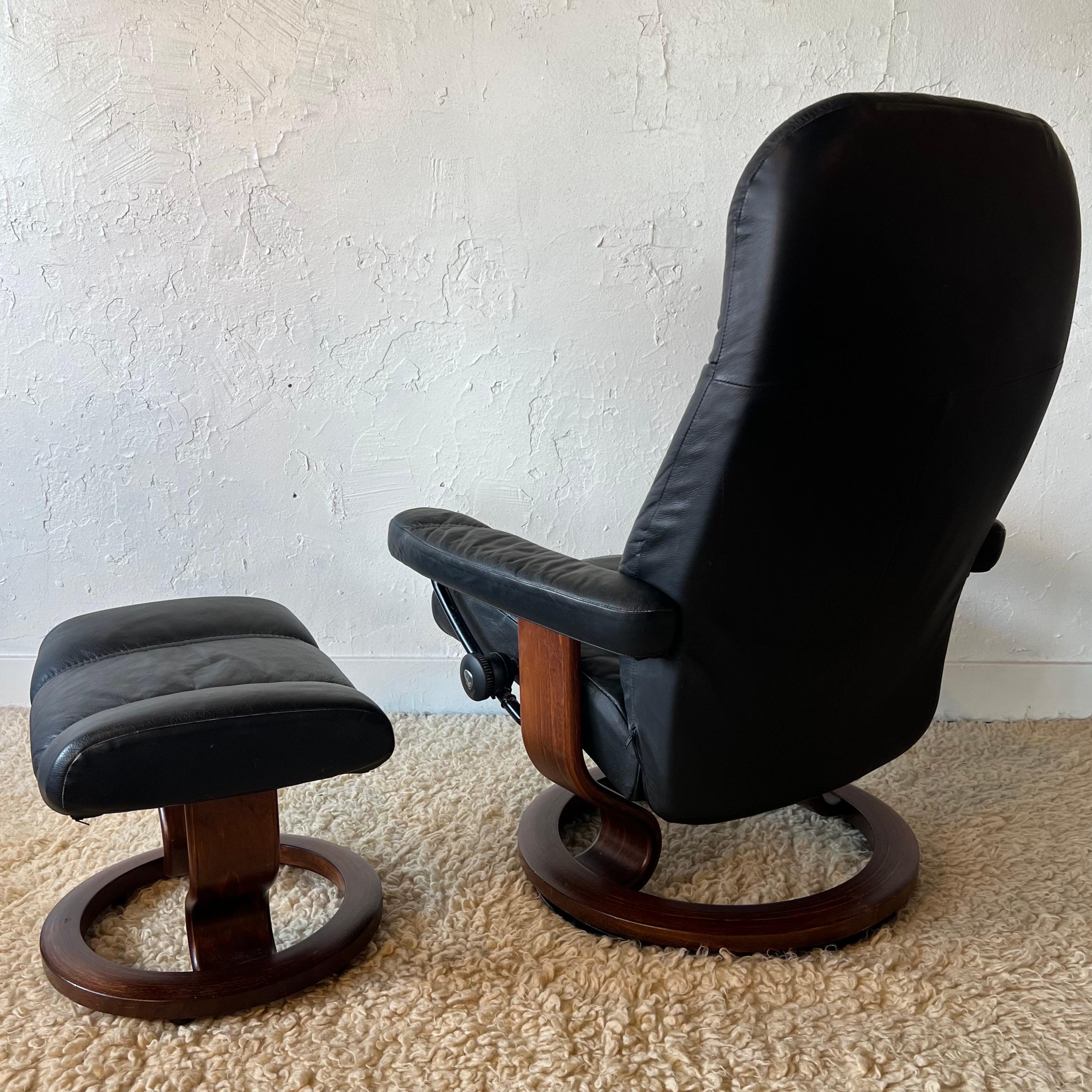 A Scandinavian style recliner and ottoman by Ekornes, their Stressless brand. With dark burgundy finished wood bases and metal frame and genuine leather upholstery, this is a comfortable black  color leather recliner on a round teak wood base that