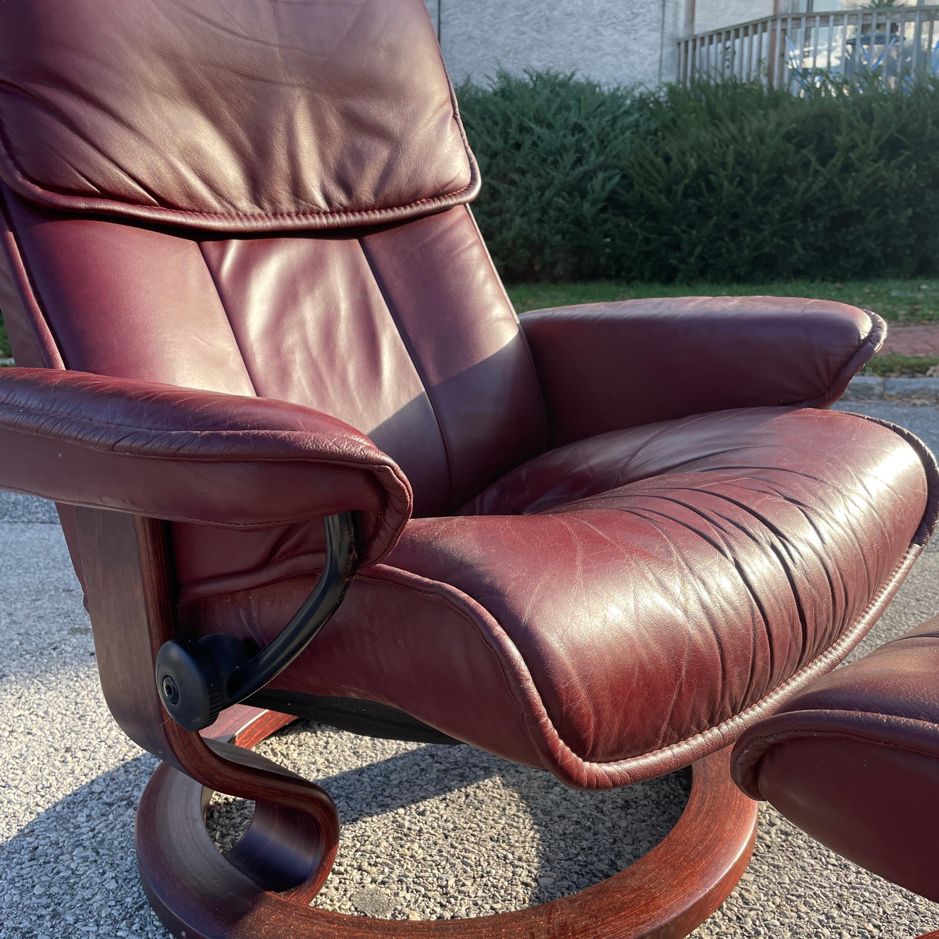 A vintage maroon leather 'Admiral' model armchair and ottoman by Ekornes Stressless of Norway. The chair has an adjustable headrest and locking recline function. It is very comfortable and the leather is in good vintage condition with only a couple