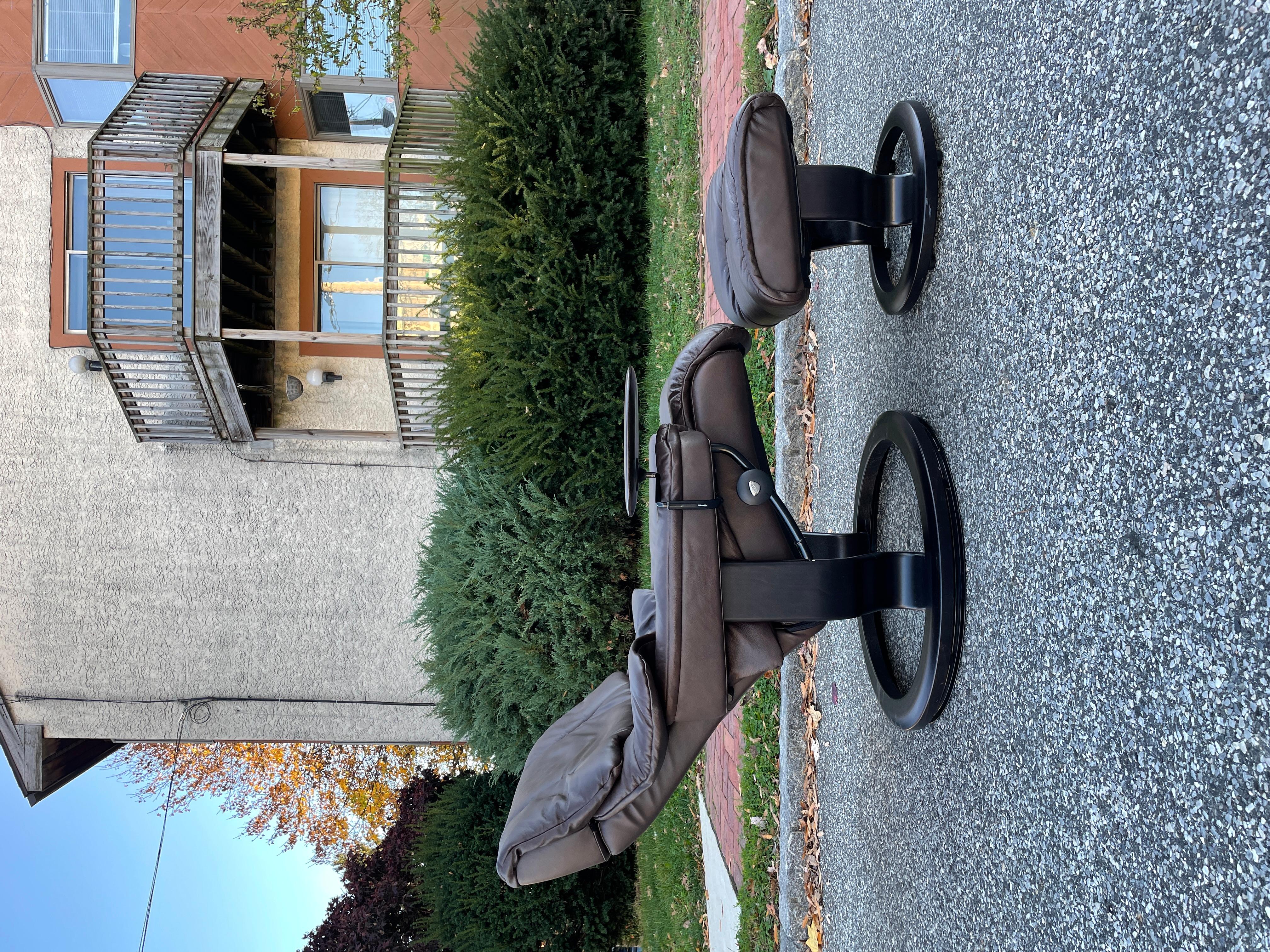 A beautiful Mid-Century Modern chocolate brown Ekornes Stressless recliner and ottoman. This recliner features a detachable wooden side table and swivel base. The head rest is adjustable. The set is barely used! It includes the original paperwork
