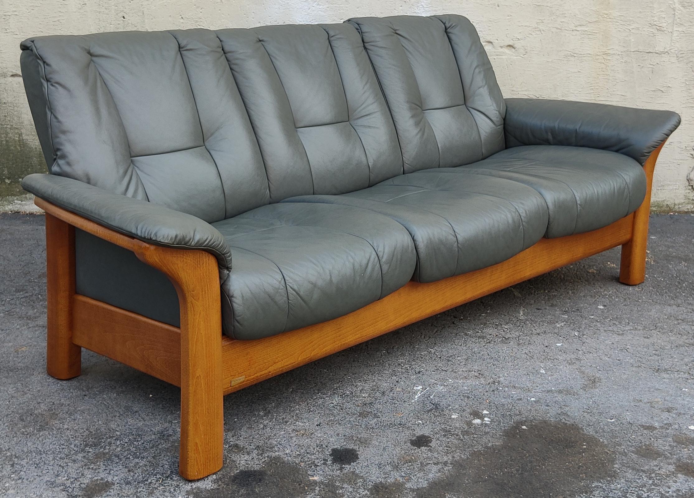 Dieses elegante und raffinierte Sofa wurde von Ekornes für ihre Marke Stressless hergestellt. Er ist aus massivem Teakholz gefertigt und mit einer sehr warmen Beize versehen, die an die berühmten Stressless-Loungesessel erinnert. Ergänzt wird die
