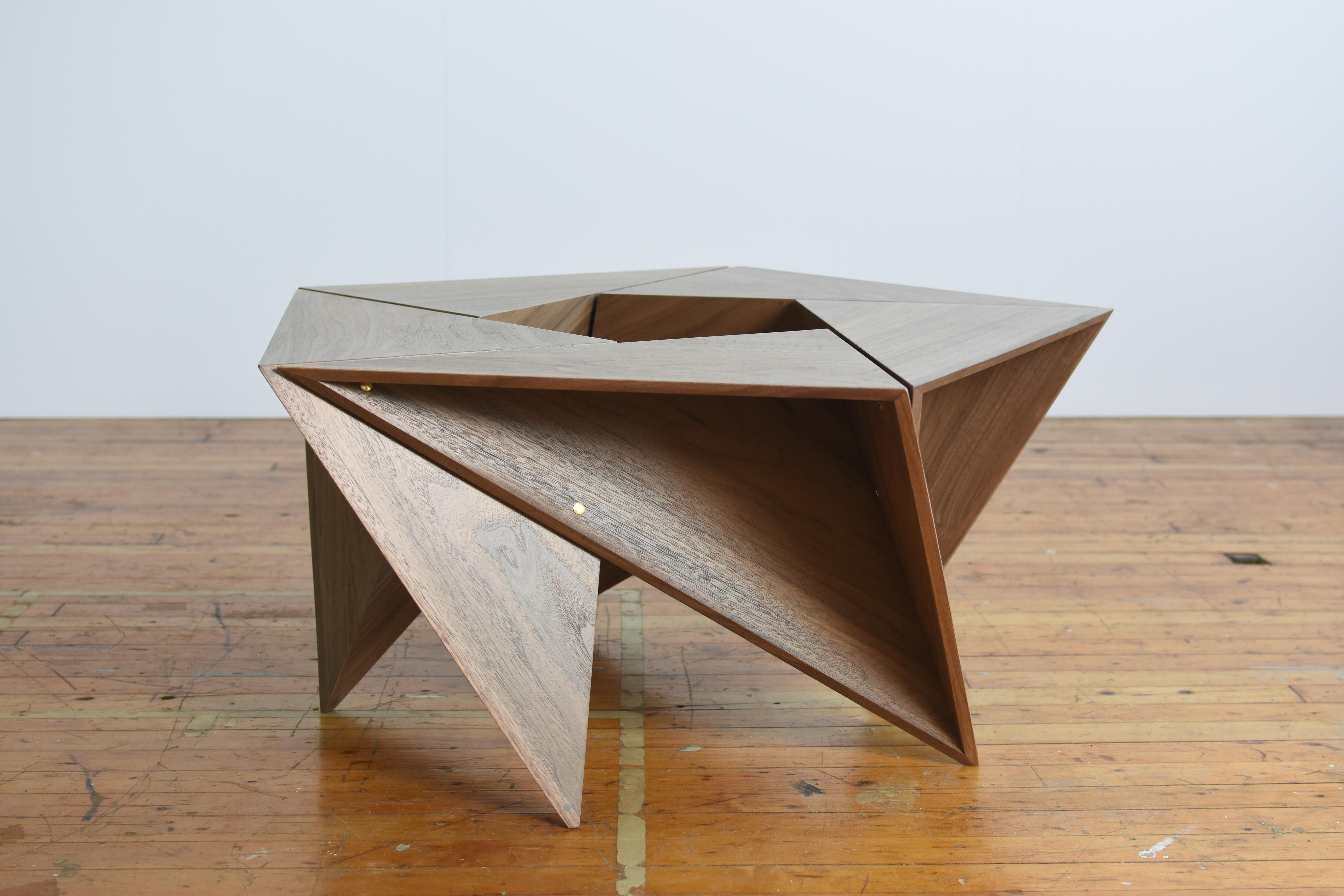 Dieser fünfeckige Tisch besteht aus 5 identischen Tetraedern mit offenen Flächen. Die mit Messingbolzen zusammengehaltene Einheit kann zerlegt und für einen kompakten Transport ineinander geschoben werden.

Das Bild hier ist eine Nussbaumsperrholz