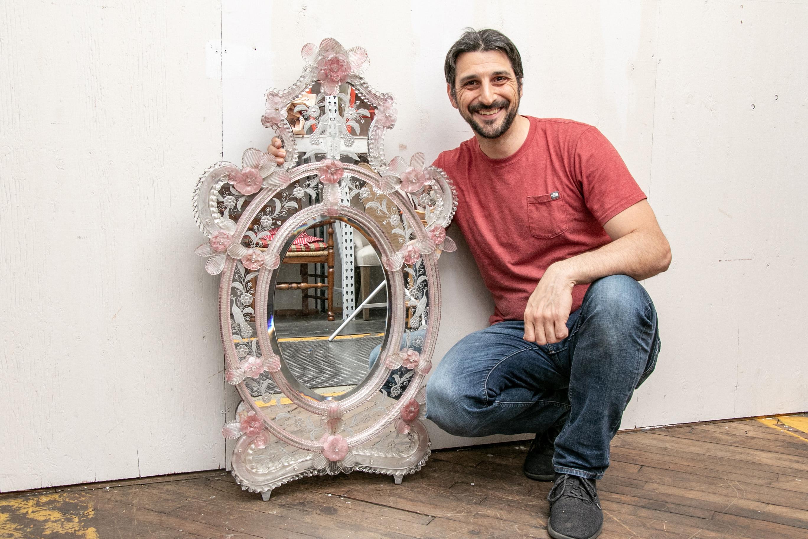 Once belonging to American Film Producer Verna Harrah. Italian oval Venetian wall mirror having clear and pink Murano floral appliqué. The surround crest and terminal etched in a peacock and flowering vine motif.

Condition: Good condition with