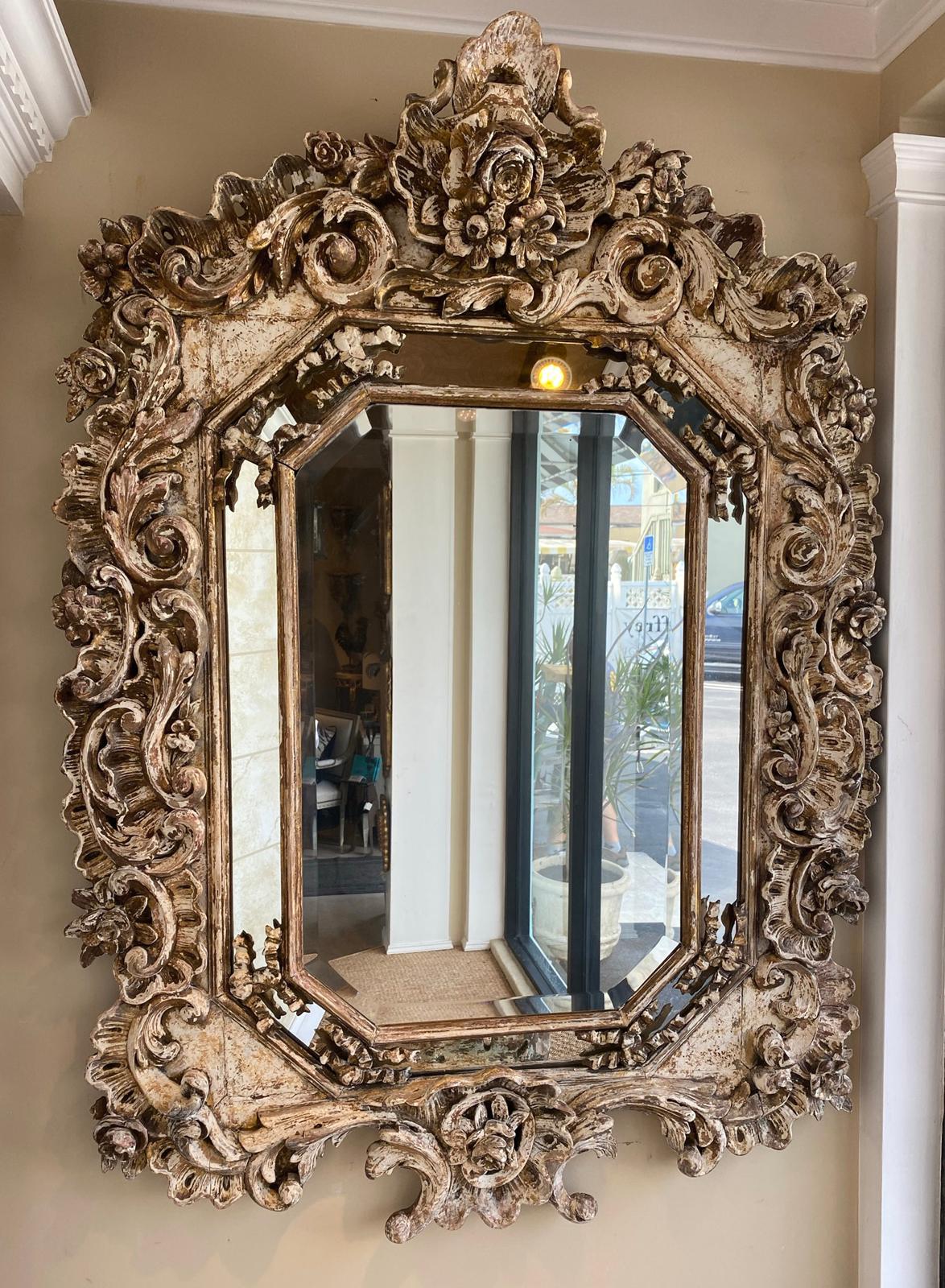 Incredibly articulated mirror, in the Rococo style; having an octagonal mirrorplate, surrounded by a mirrored relief border, inset with ribbons, framed in expansive and bountiful decorations of scrolling acanthus, rose blossoms, C-scrolls, and