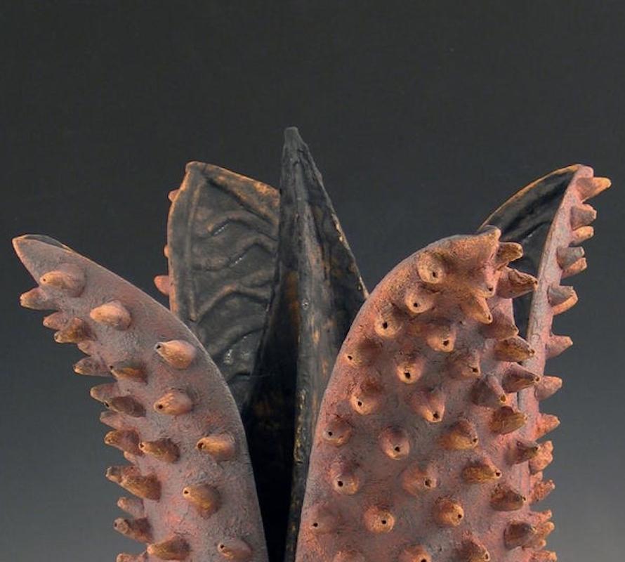 Bristled Beauty,  a phantasmic ceramic flower features a stark, dark, black interior with iron red petals studded with conical ornamentation. Always looking for new materials and methods, the artist has made sculpture in such diverse materials as