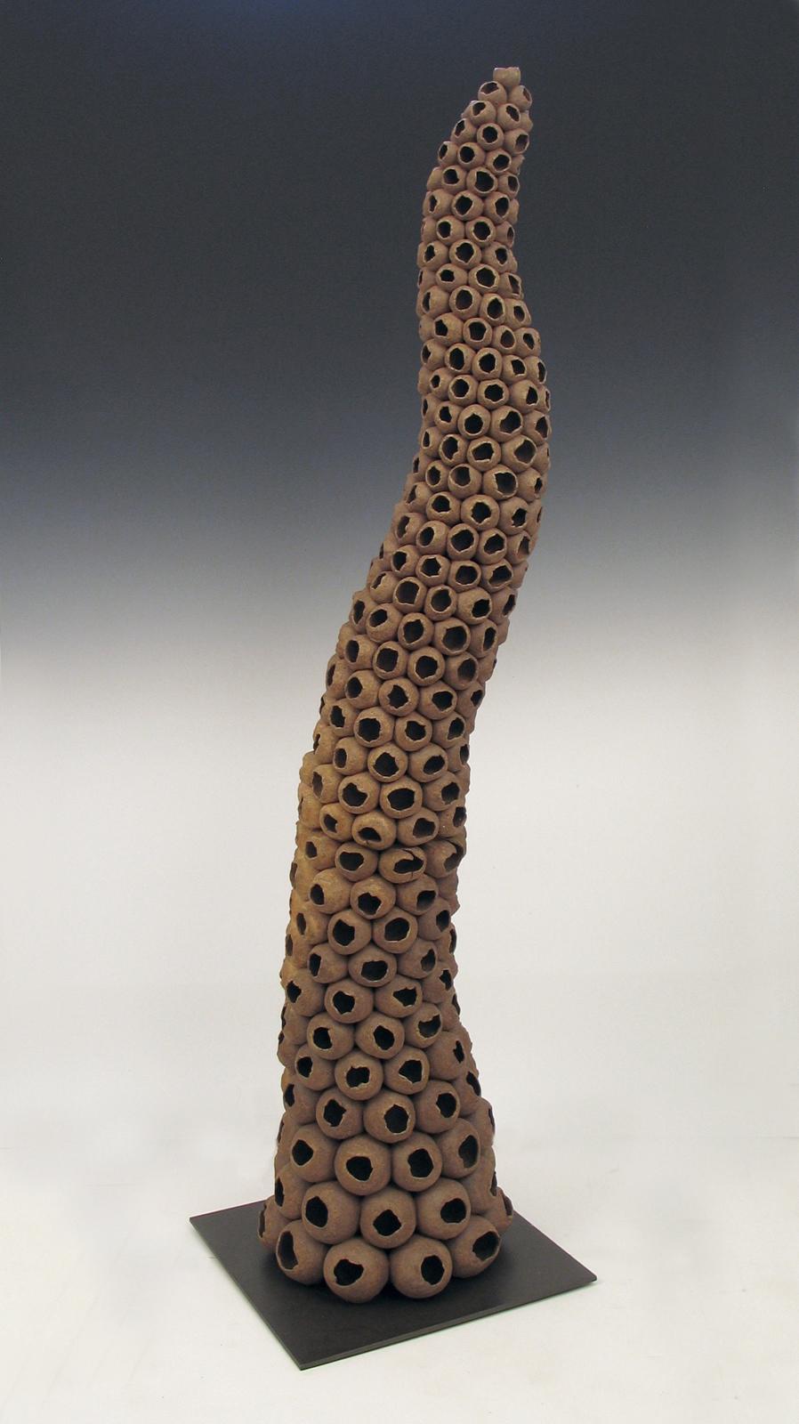“Depleted”, natural colored ceramic seedpods bloom on an undulating form. Always looking for new materials and methods, the artist has made sculpture in such diverse materials as wood, metal, concrete, encaustic and ceramic, maintaining a view of