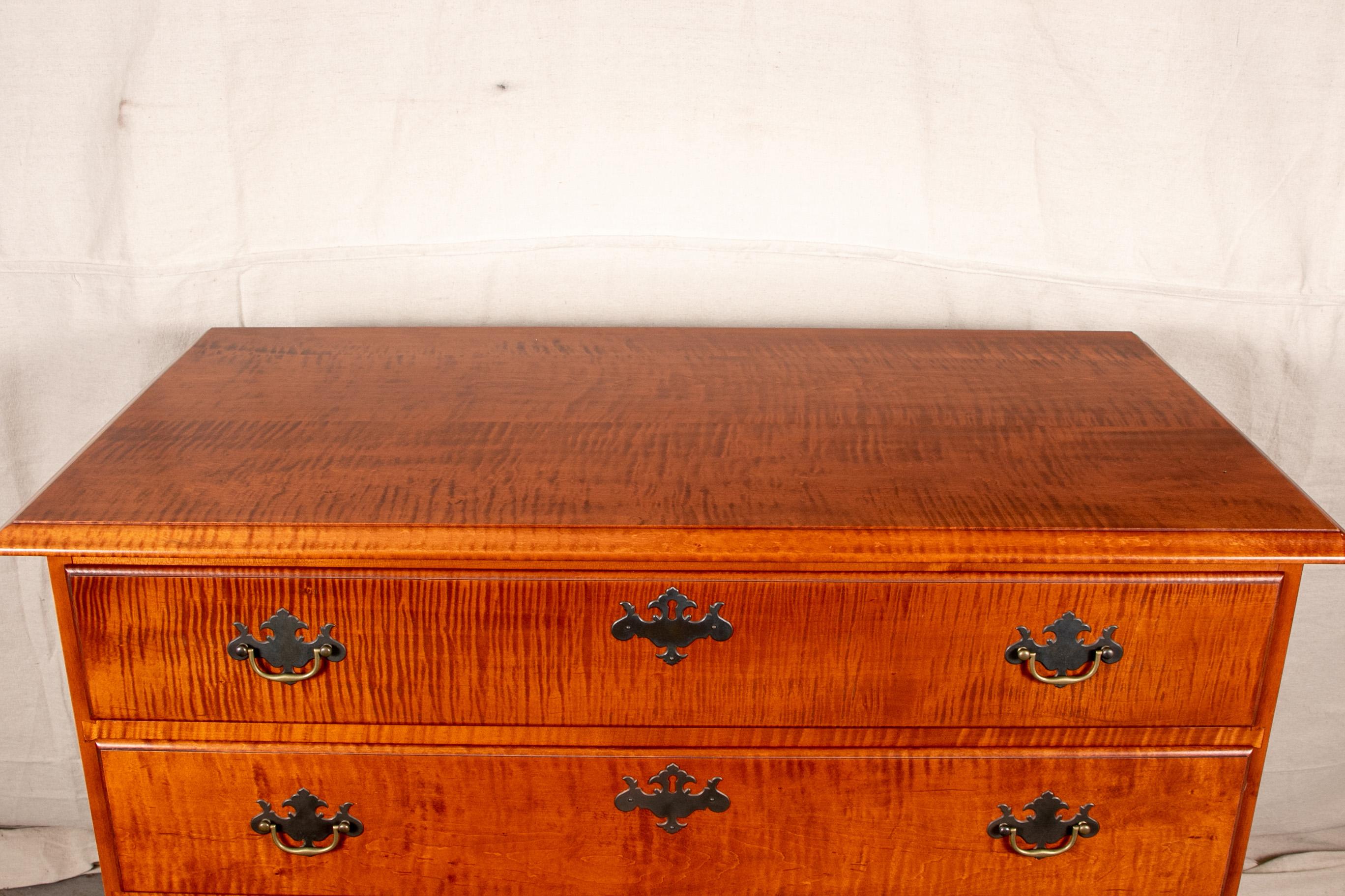 Eldred Wheeler [Hingham, MA] chest of four drawers, tiger maple with pine secondary, rectangular bevelled top over four drawers of graduated sizes, supported on bracket feet with central carved fan in reverse along skirt, brass bale handles and